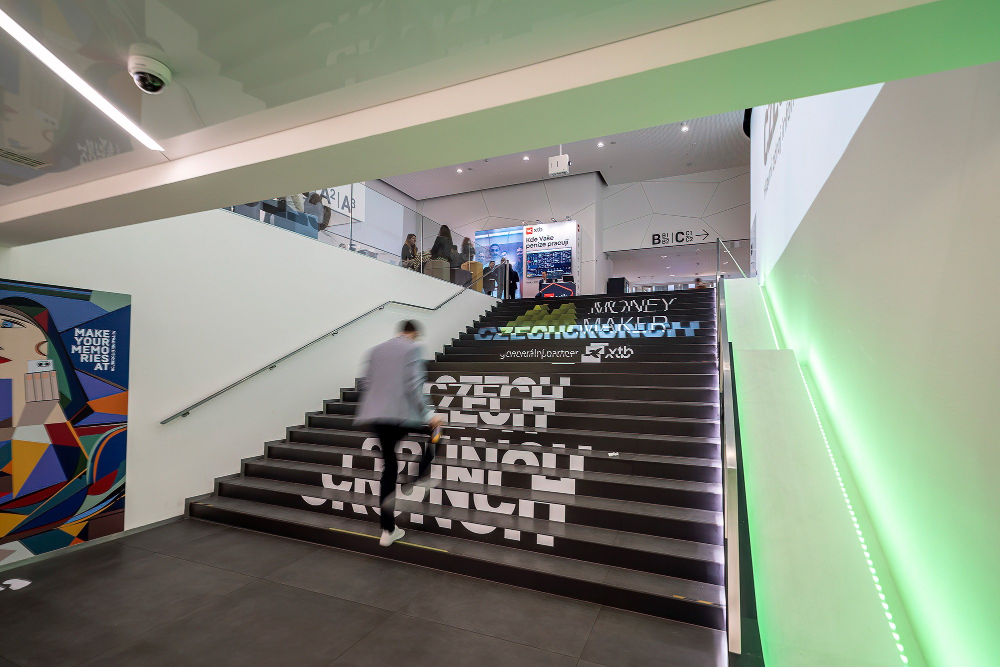 Attendee walking up branded stairs at the Money Maker business conference by CzechCrunch in Prague, showcasing event branding and venue atmosphere.
