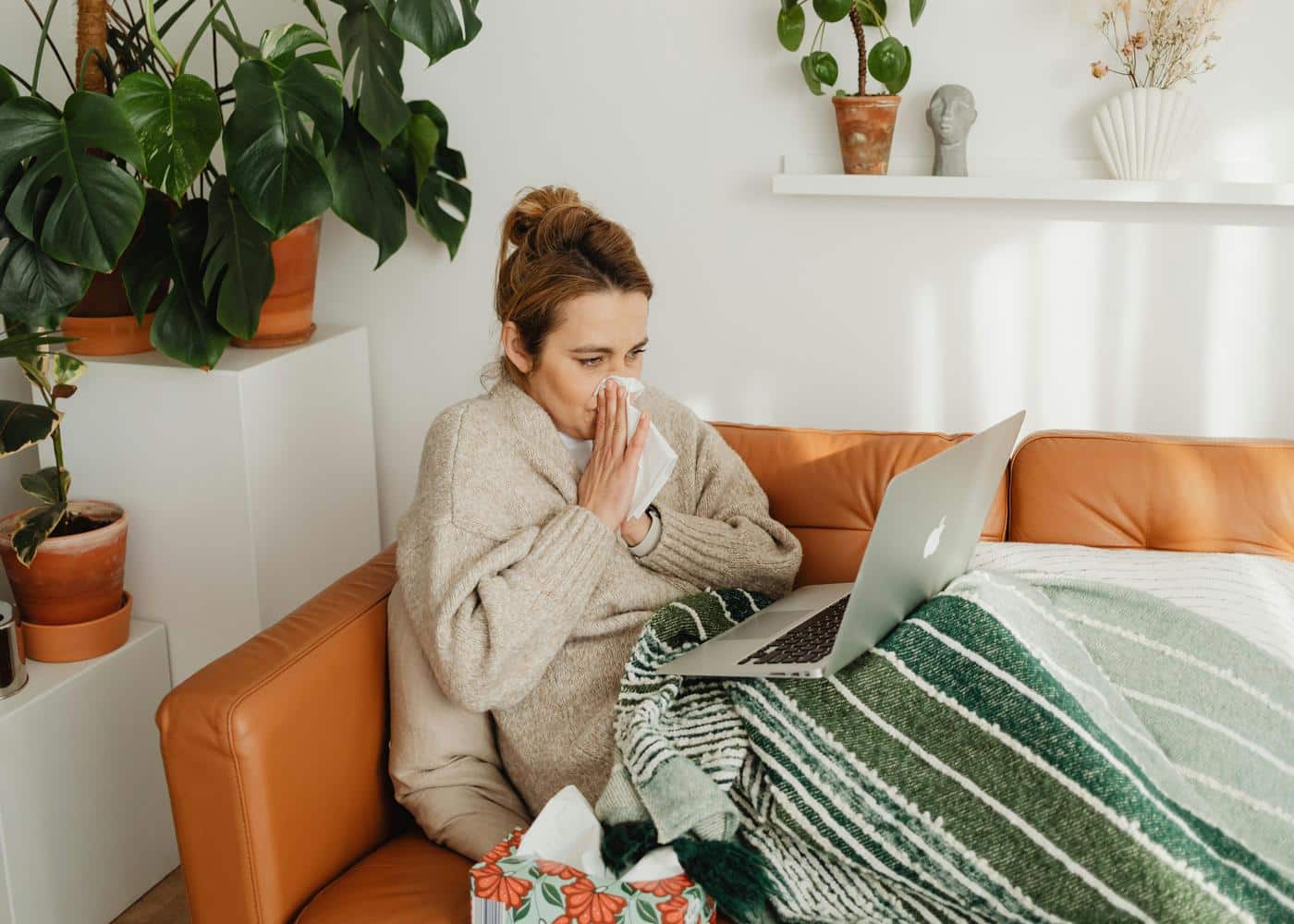 Woman sat on a couch and Googling health symptoms while blowing her nose