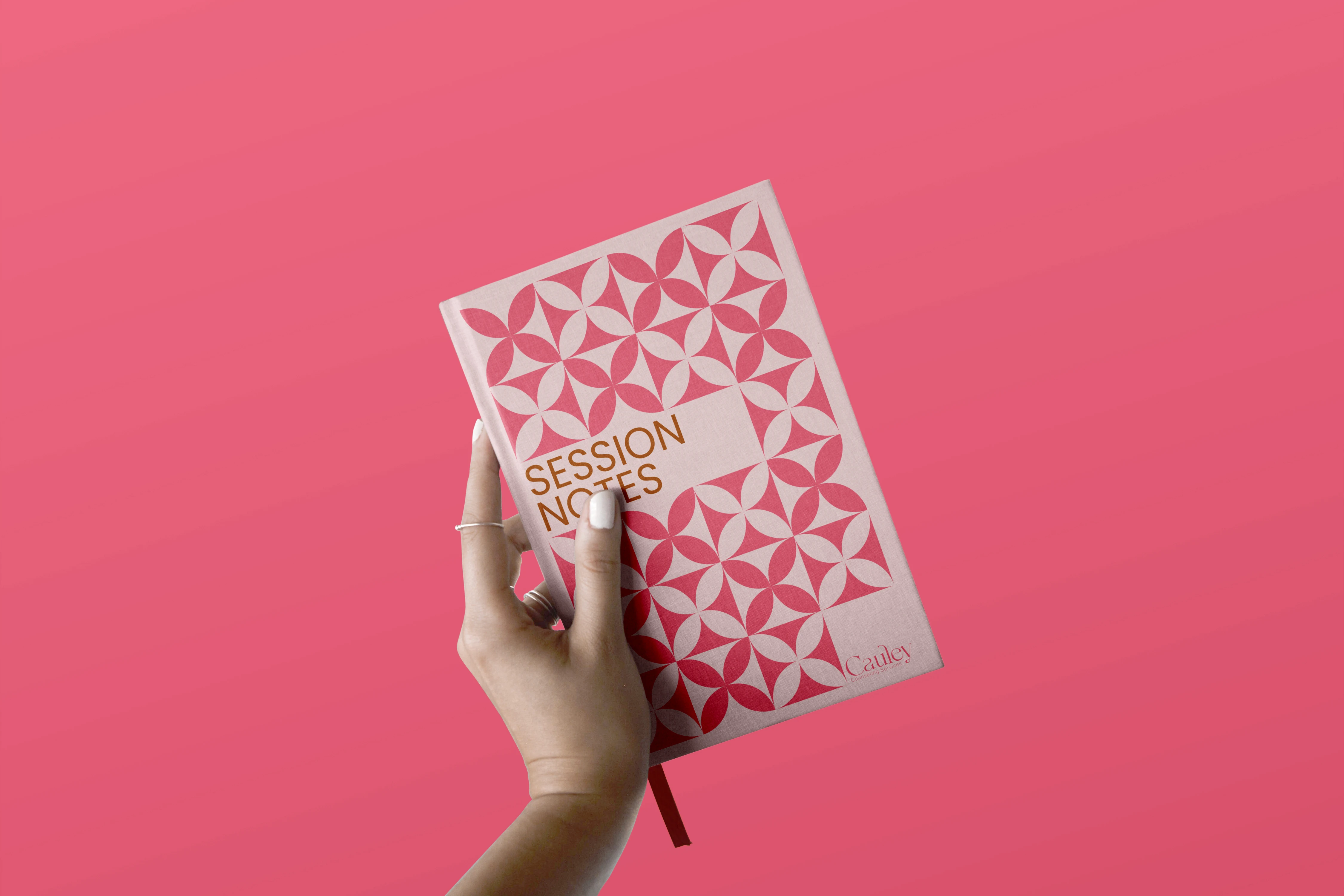 A hand holds a notebook against a soft pink background, showcasing session notes for Cauley