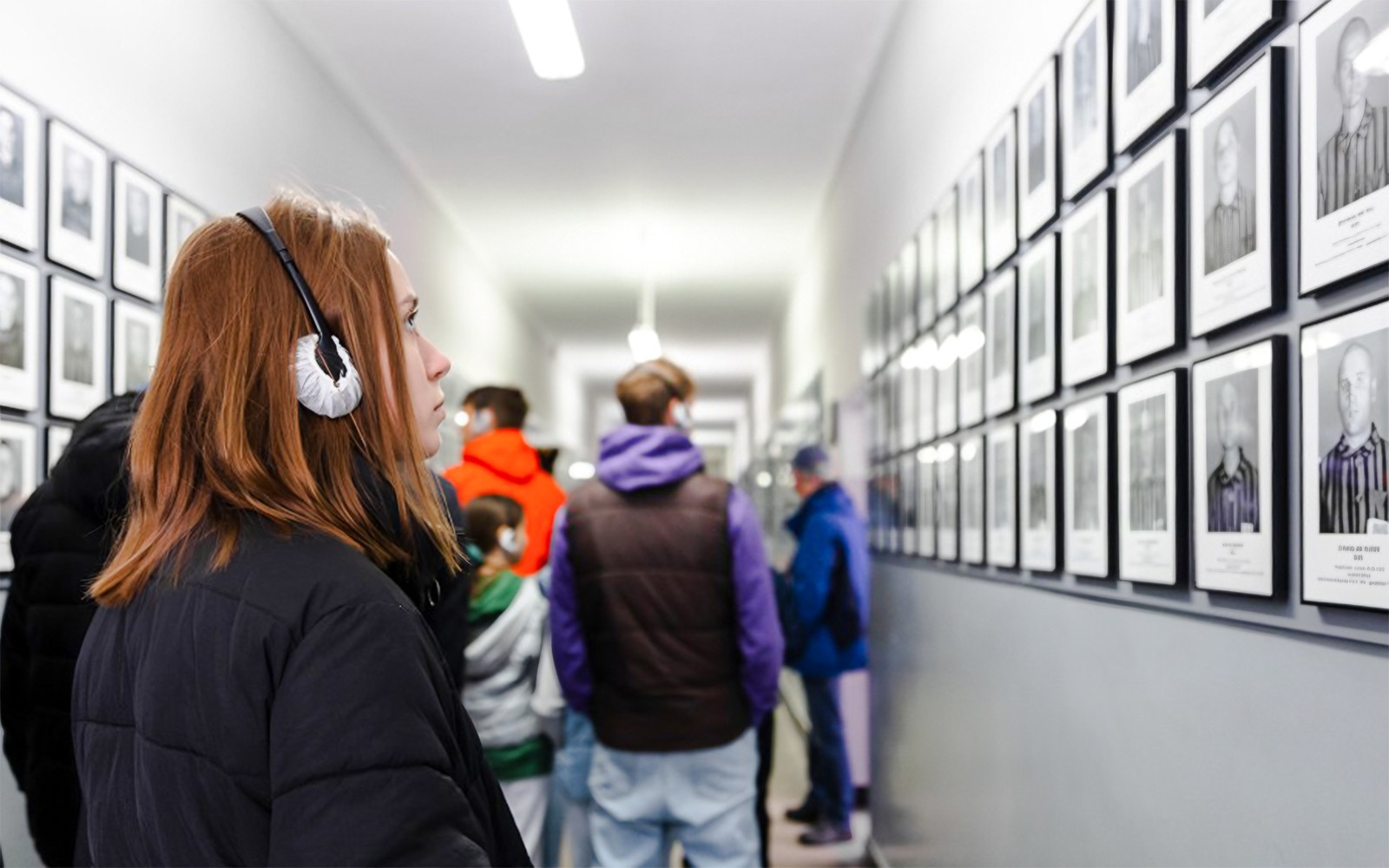 Gestur með hljóðleiðsögn á Auschwitz-Birkenau minnisvarðanum, skoðar fangamyndir á gangi.