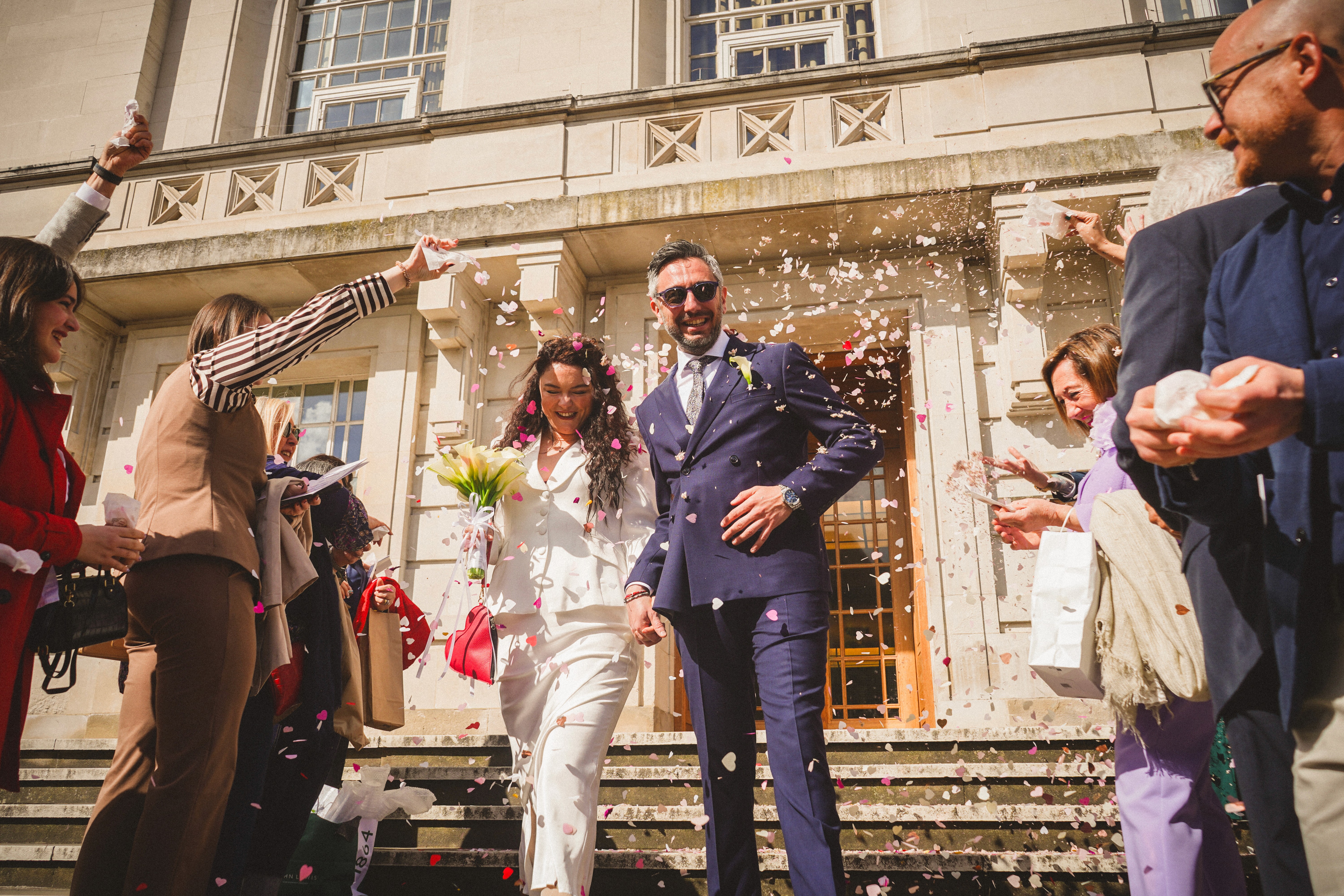 A newly-married couple is covered in coffetti while walking down steps at a wedding in London