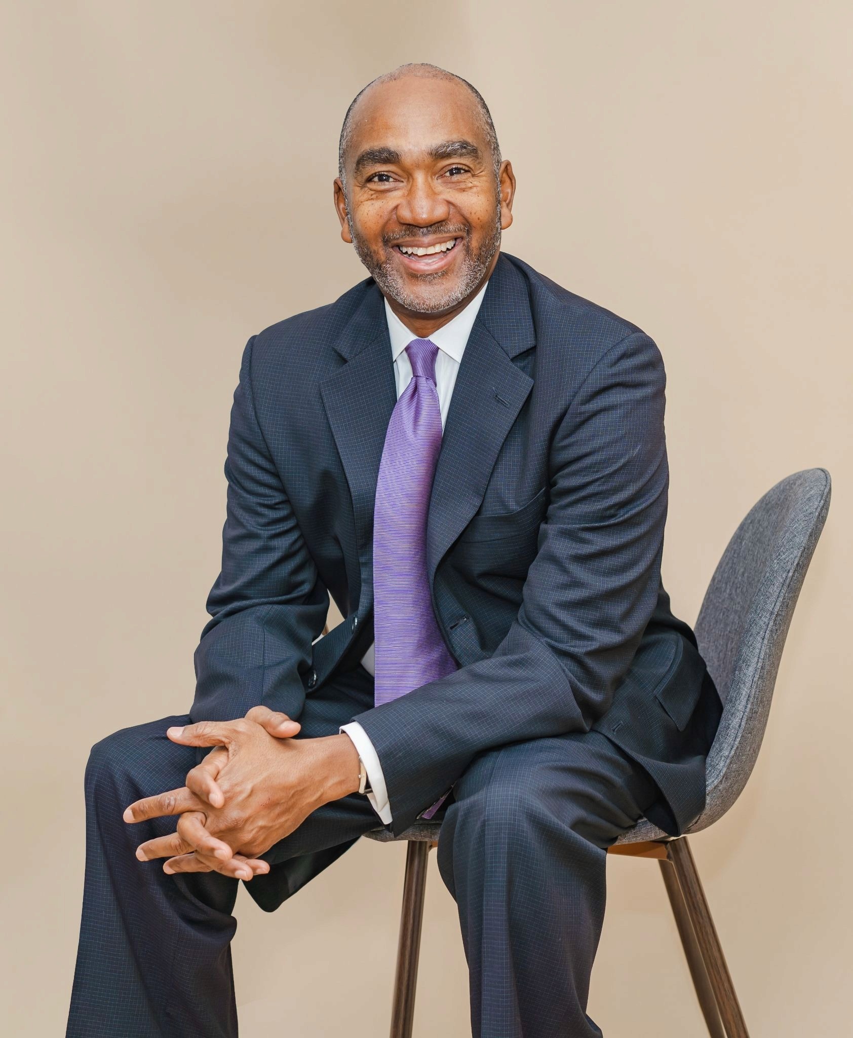 Michael Bernard Allen seated in a suit, smiling during a professional portrait.