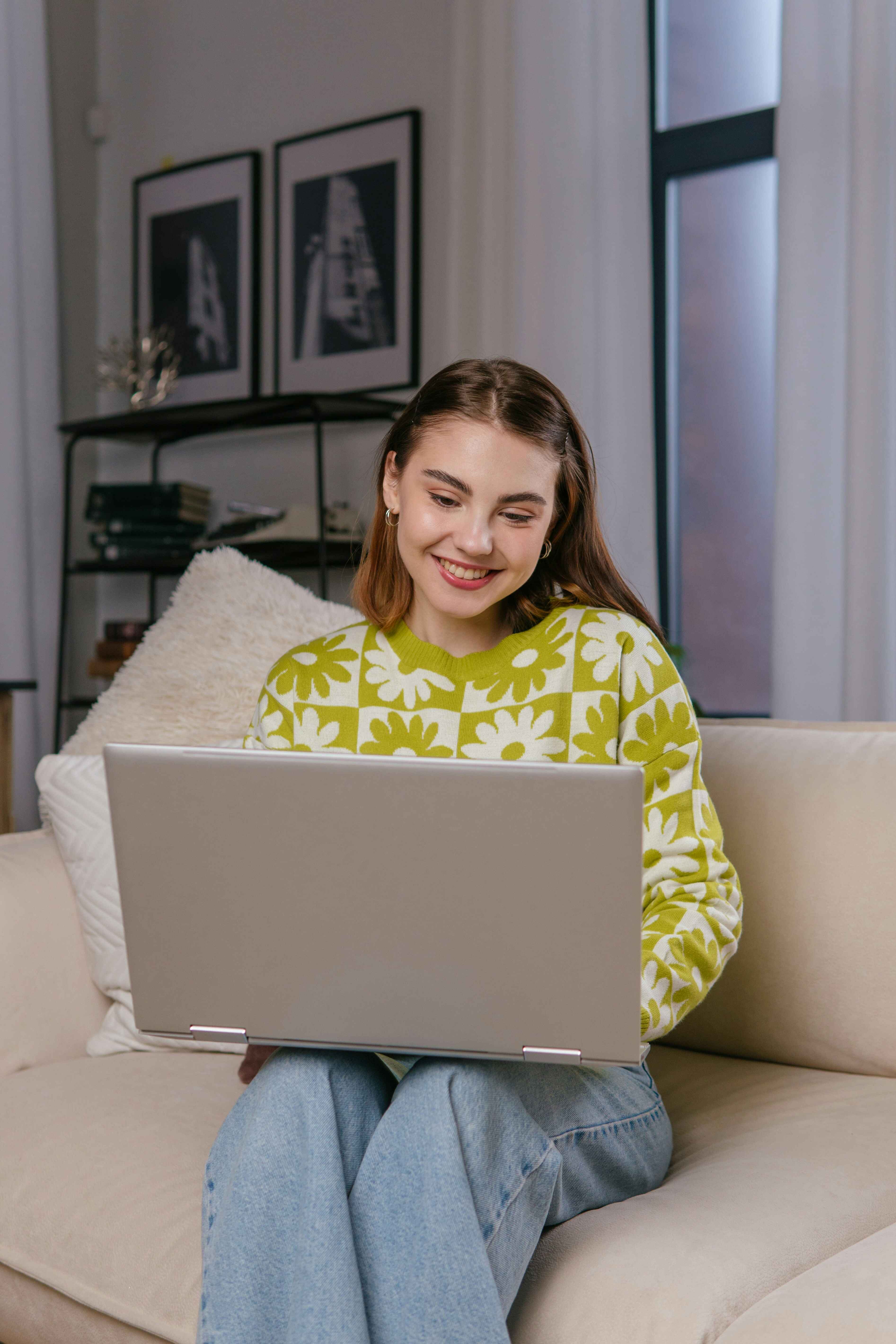 A woman sitting on a couch, using a laptop for online therapy at the Family Time Center.