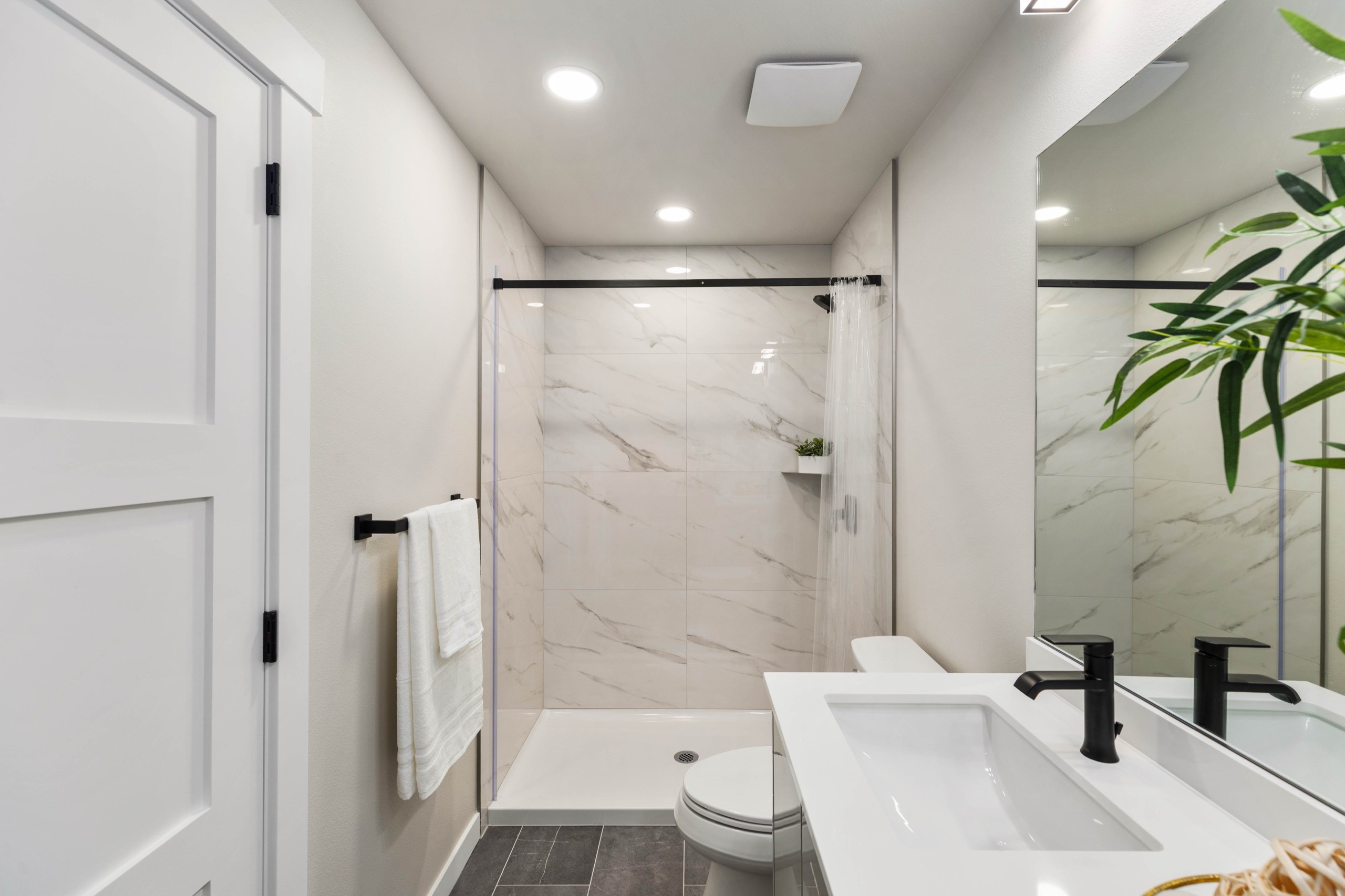 Elegant luxury ensuite bathroom with full marble slab walk-in shower, double white rectangular vessel sinks, black matte fixtures, and dark wood-look tile floor