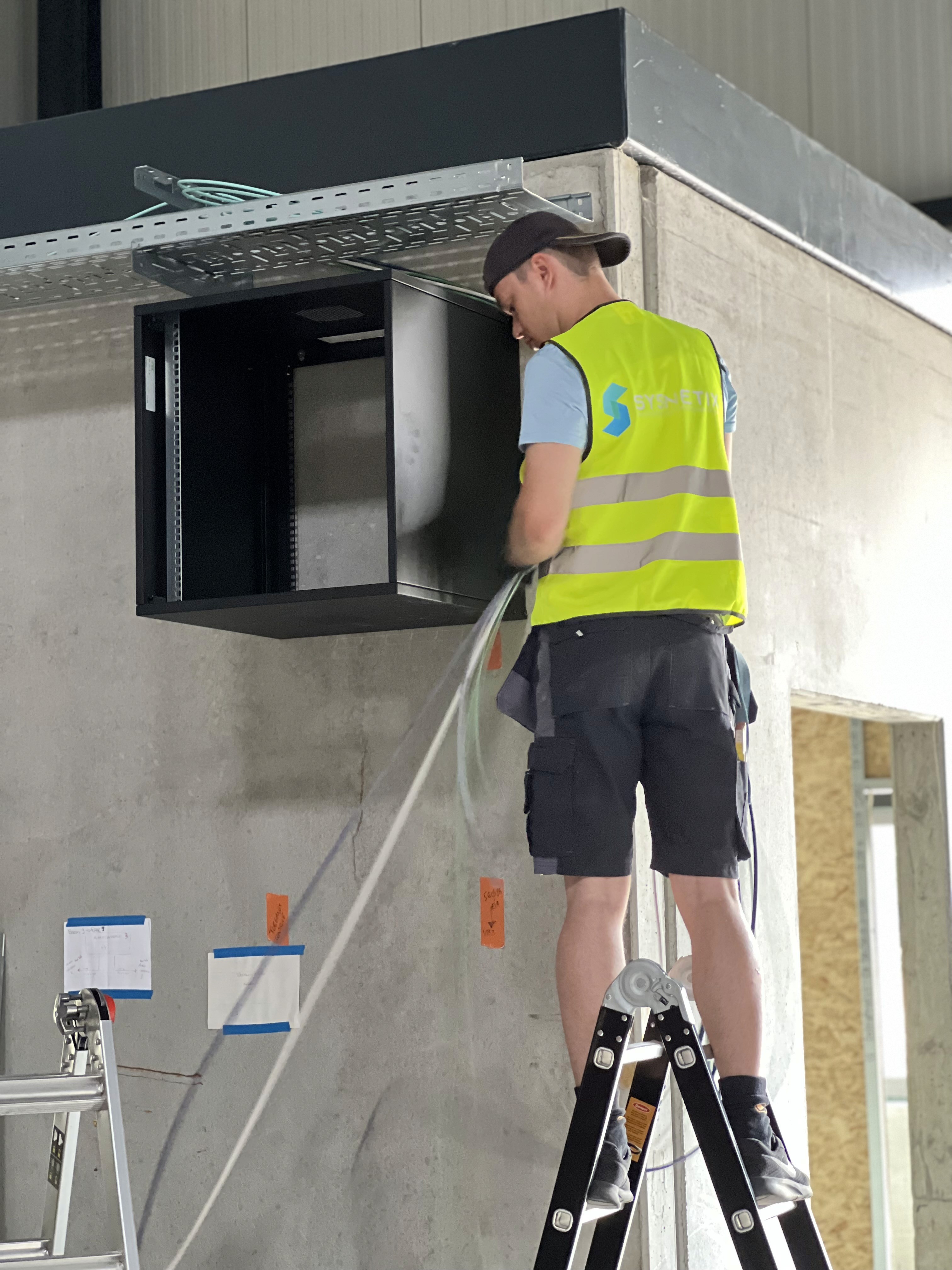 Technicus op een ladder bij een netwerkkast van Nearfield