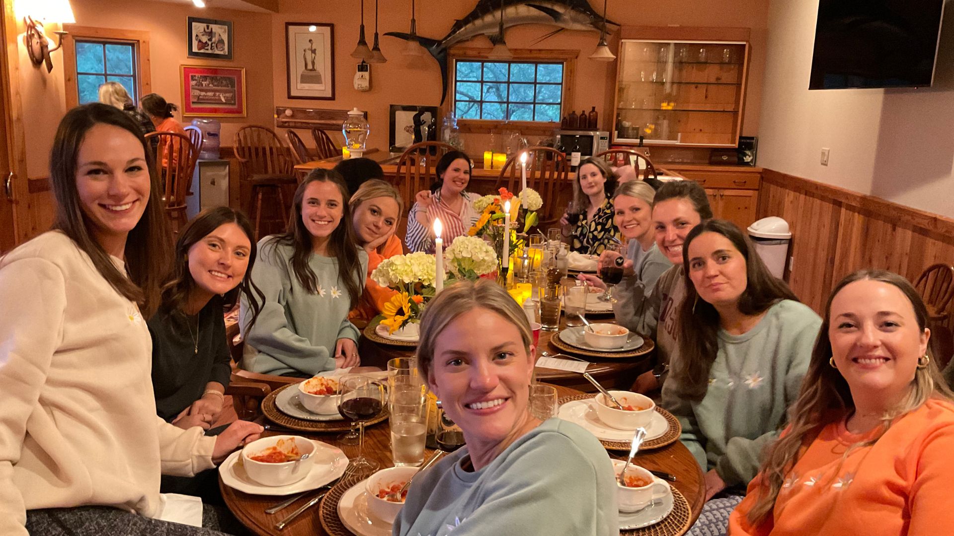 Wooden outdoor table set with multiple plates of food, including dips, salads, potatoes with cheese, and glasses of water, with hands reaching in to eat.