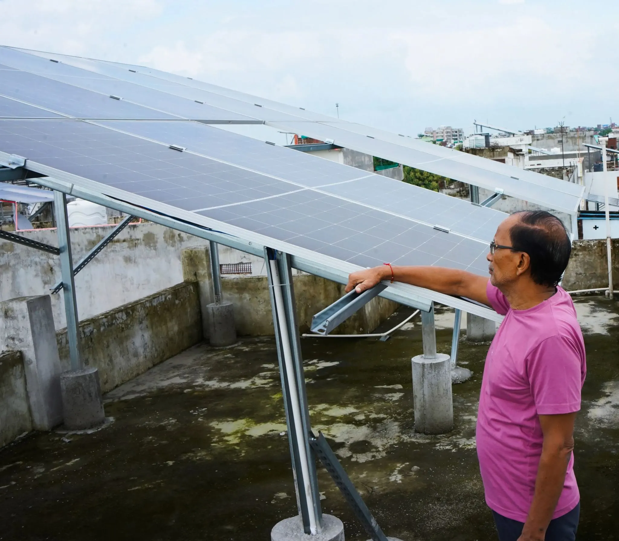 Man in a pink shirt pointing at solar panels installed on his rooftop