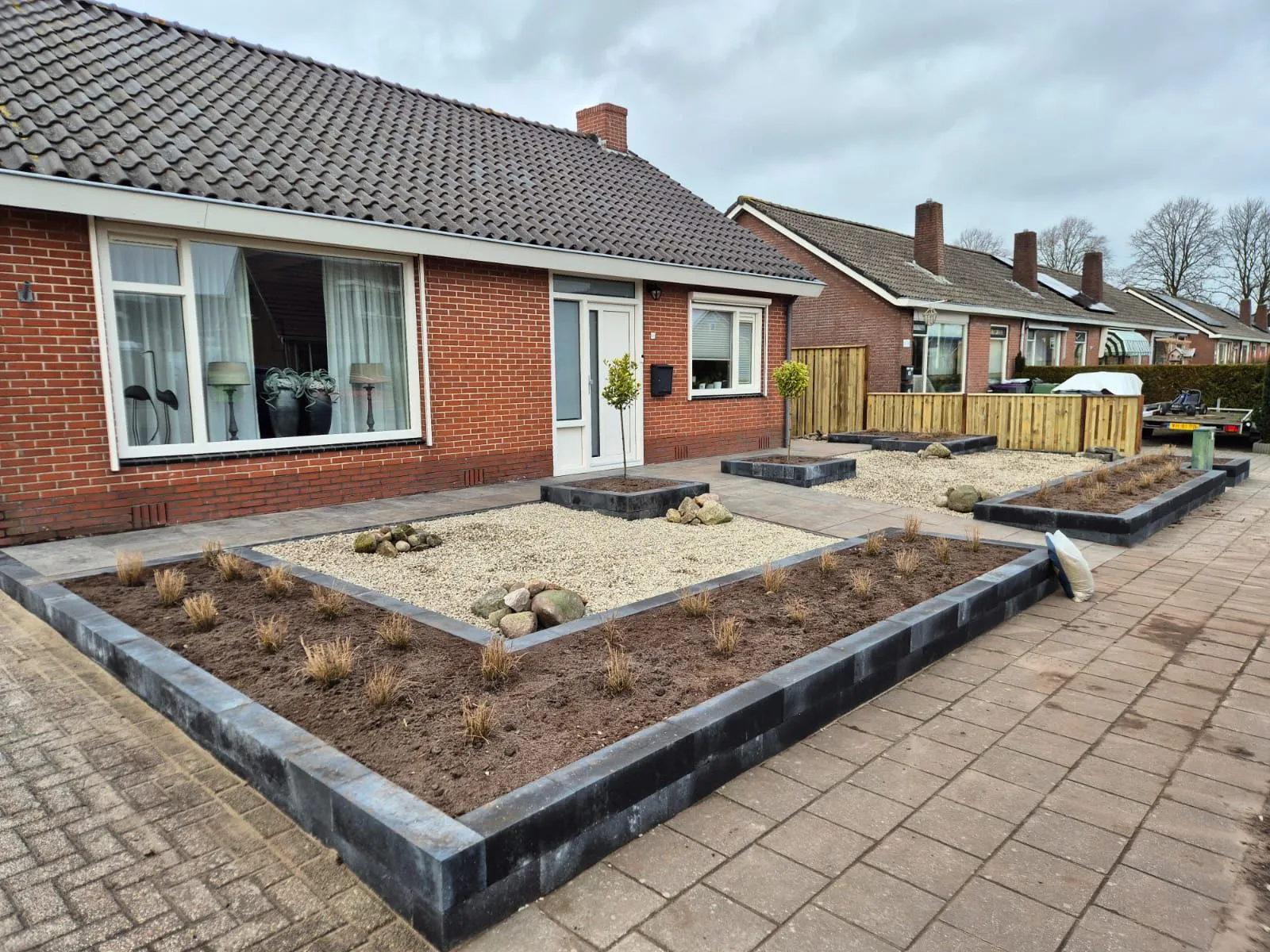 Onderhoudsarme voortuin met verhoogde plantvakken, grind als bodembedekker en twee kleine bomen bij een rijtjeshuis in Harkema.