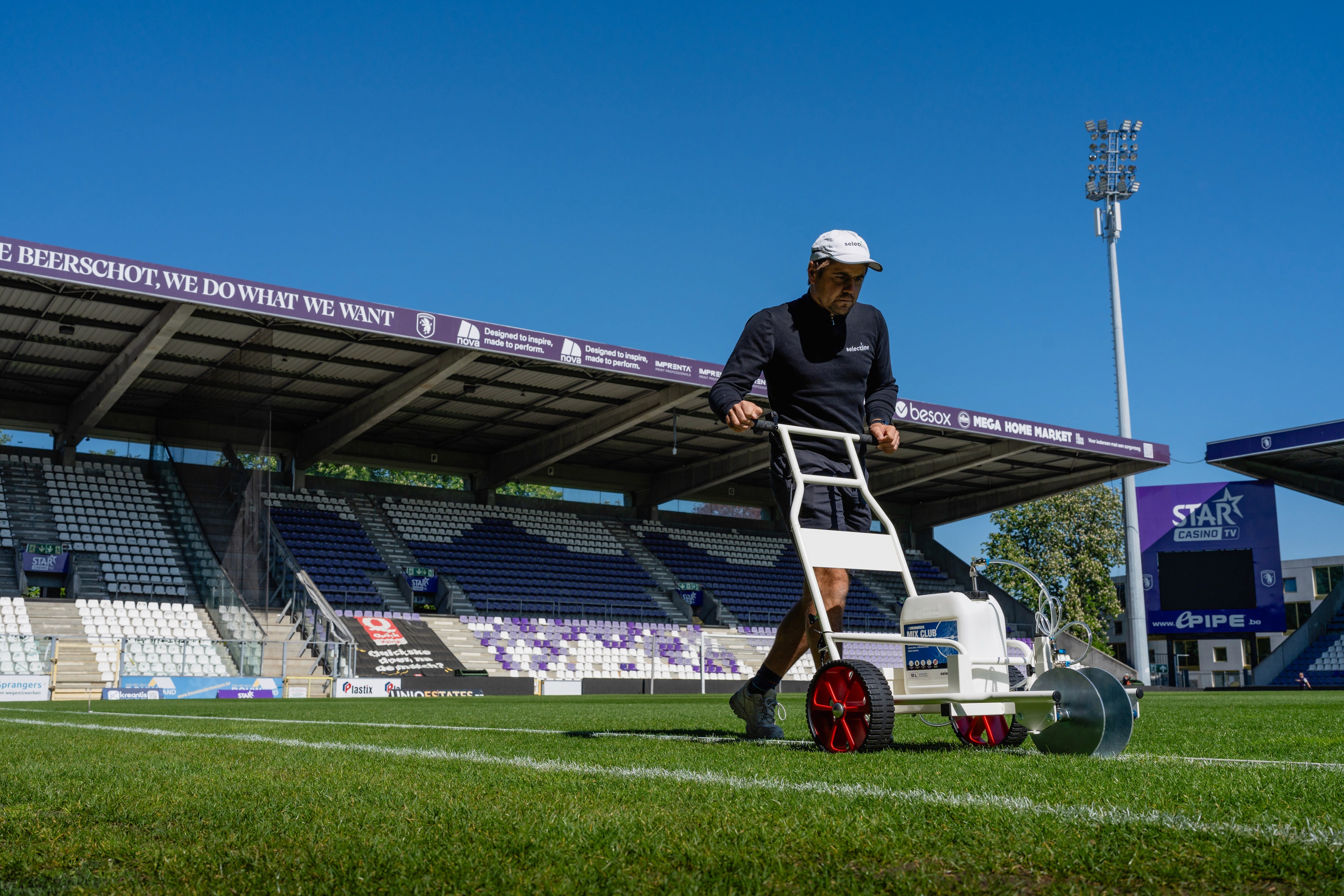 Selectlijn lijnmachine in actie op een grasveld, witte lijnen vers aangebracht.