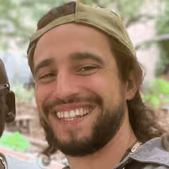Close-up portrait of a freckled woman with soft pink hair and star earring, natural light, white tank top.