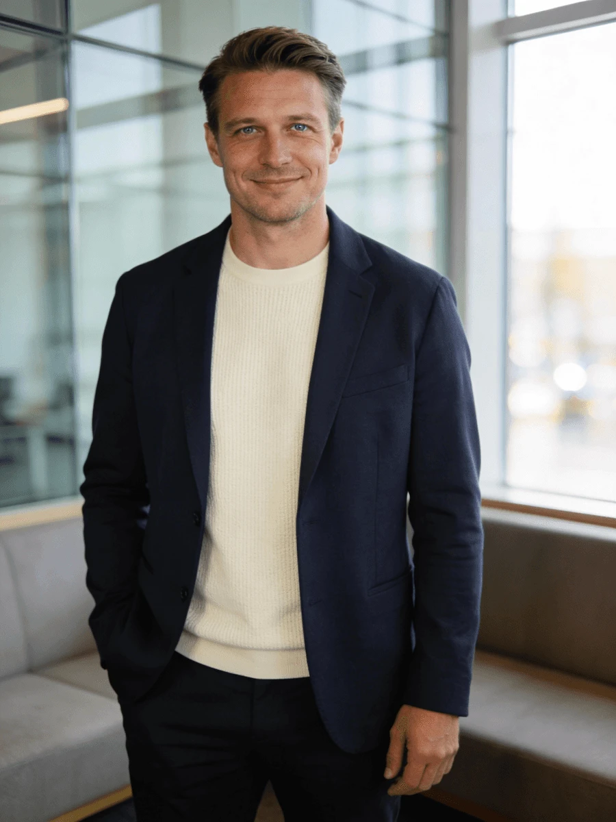 Team member in a navy blazer and cream sweater, smiling in a bright modern office