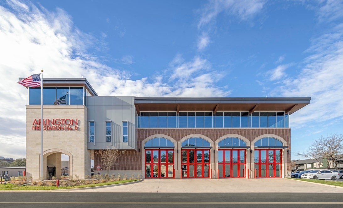 Front exterior of Arlington Fire Station No. 8 with red bay doors and stone signage, by Parkhill and Martinez Architects
