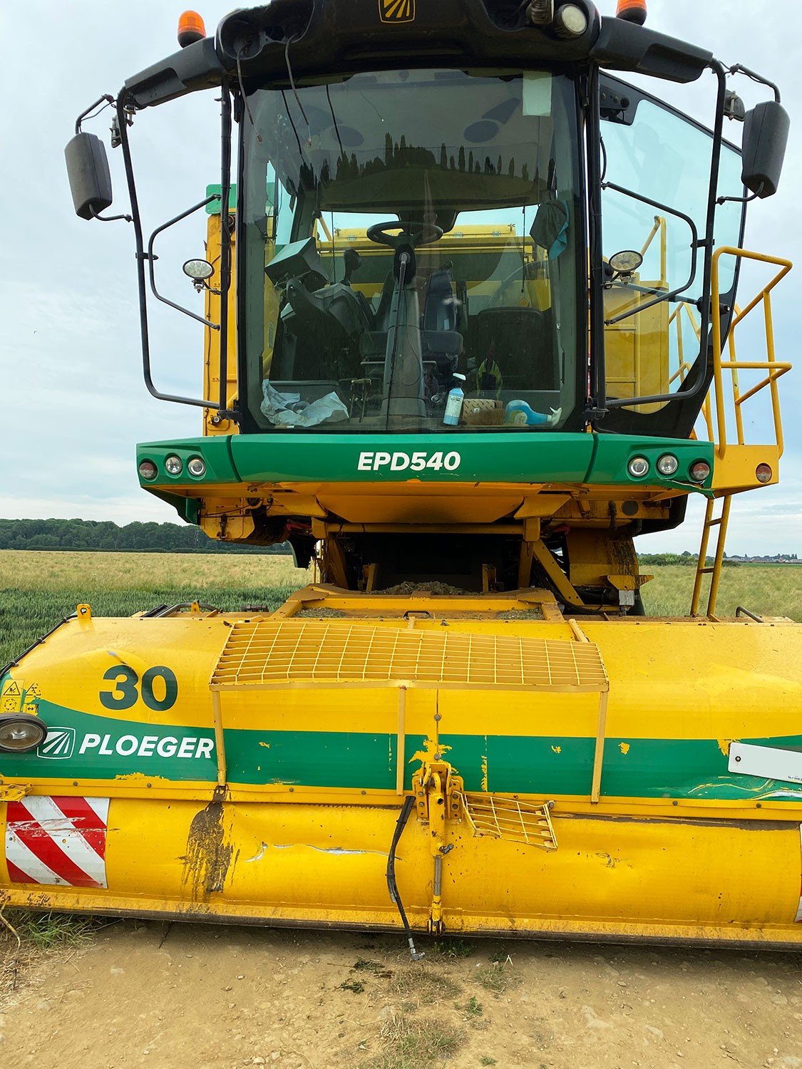 Front view of damage sustained to a Ploeger harvester. The vehicle is bright yellow and green and is in a field