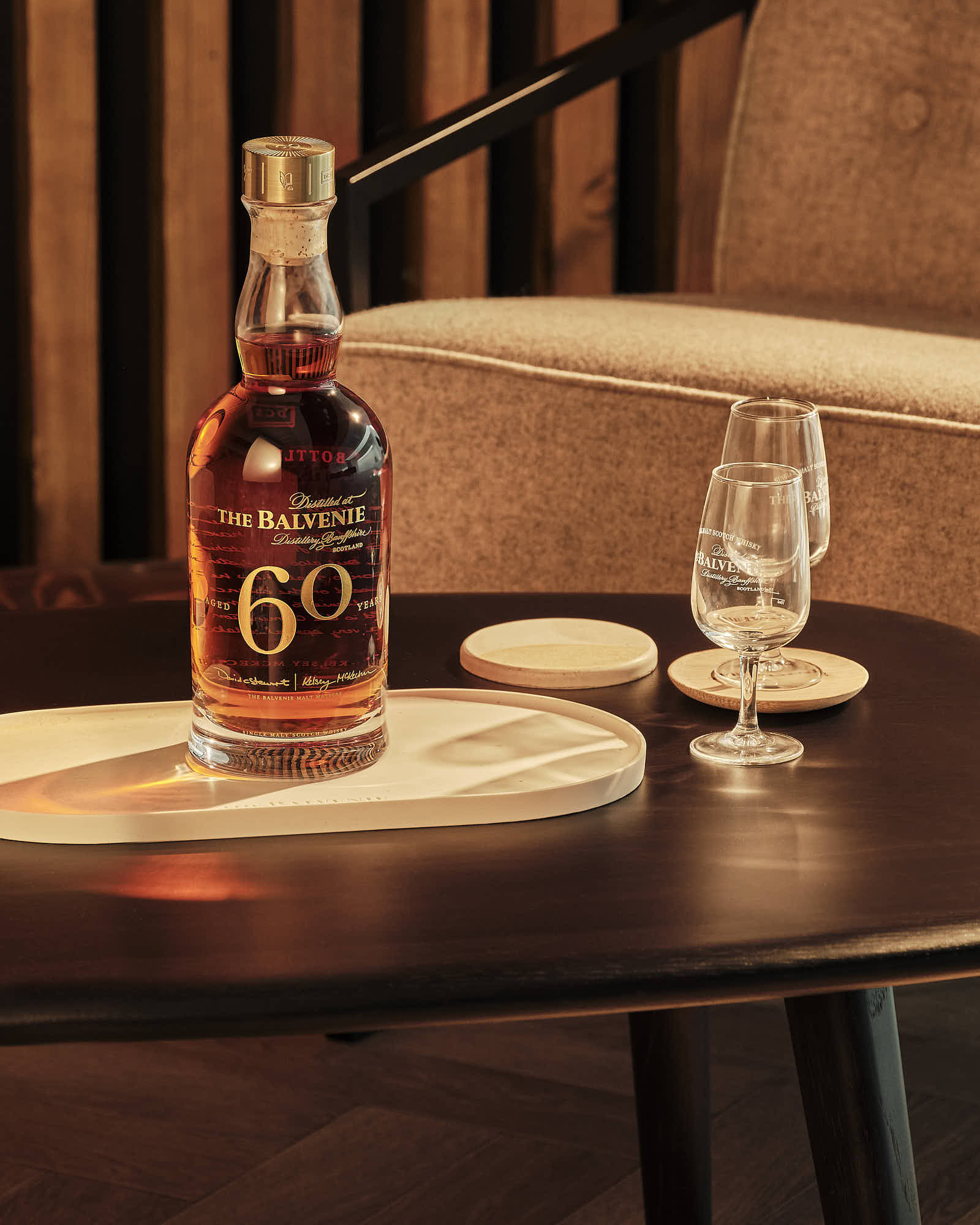 A bottle of brown liquor on a table next to a glass, with soft lighting and a cozy atmosphere.