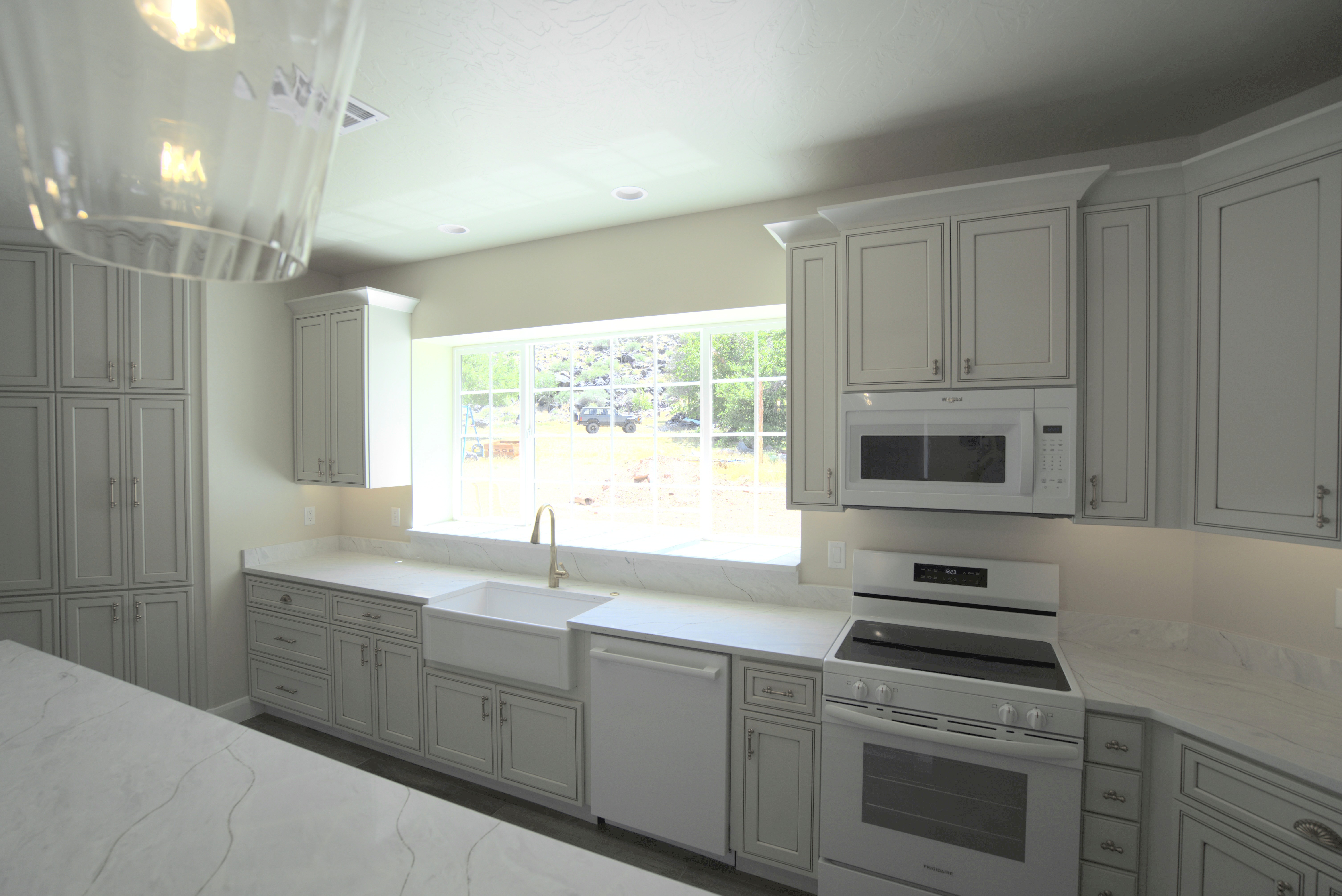 Kitchen in a custom home in Southern Utah with white cabinetry and appliances, a large gridded window, and a farmhouse sink.