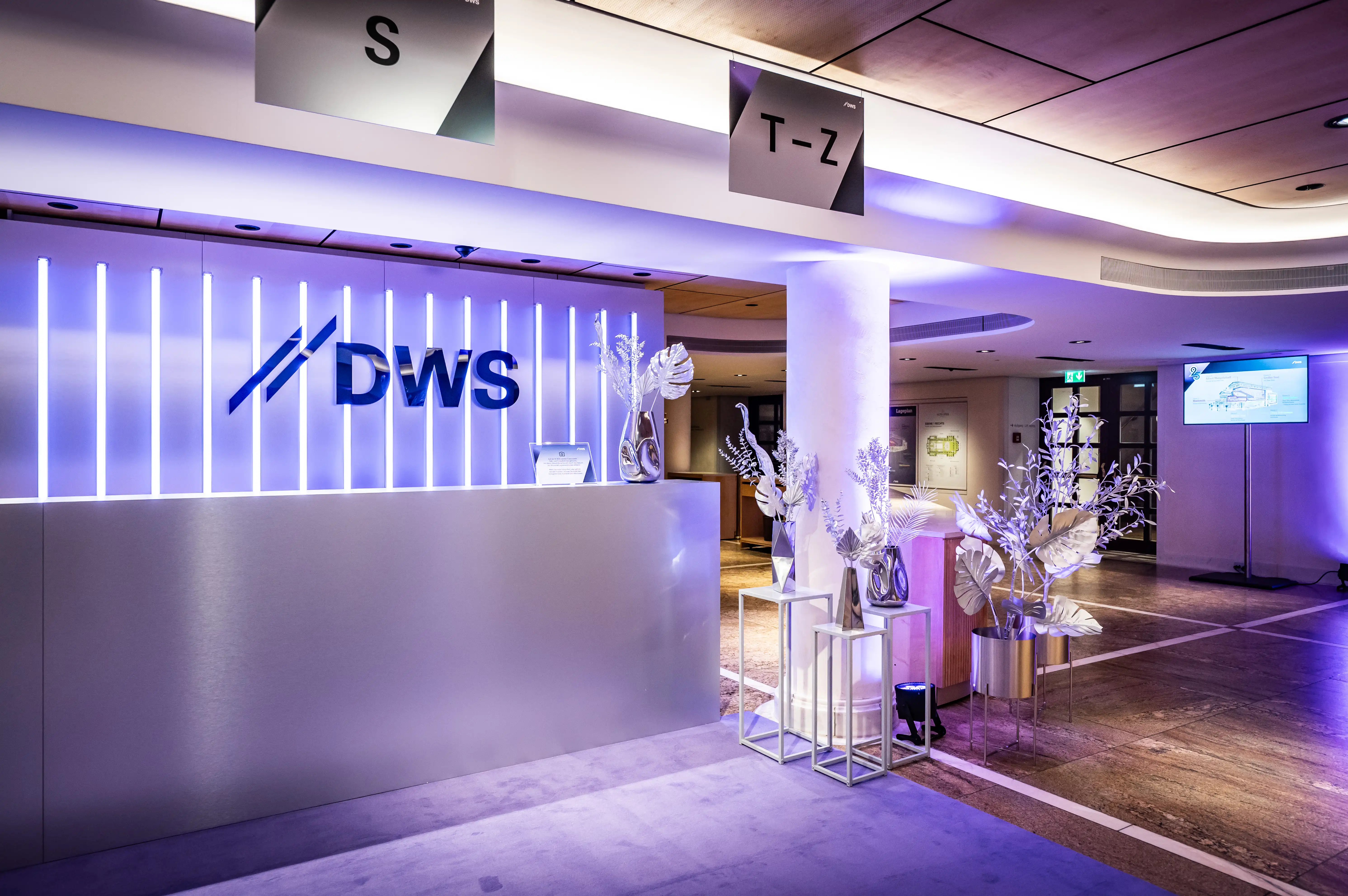 DWS logo wall with vertical light lines above the check-in counter with silver plants.