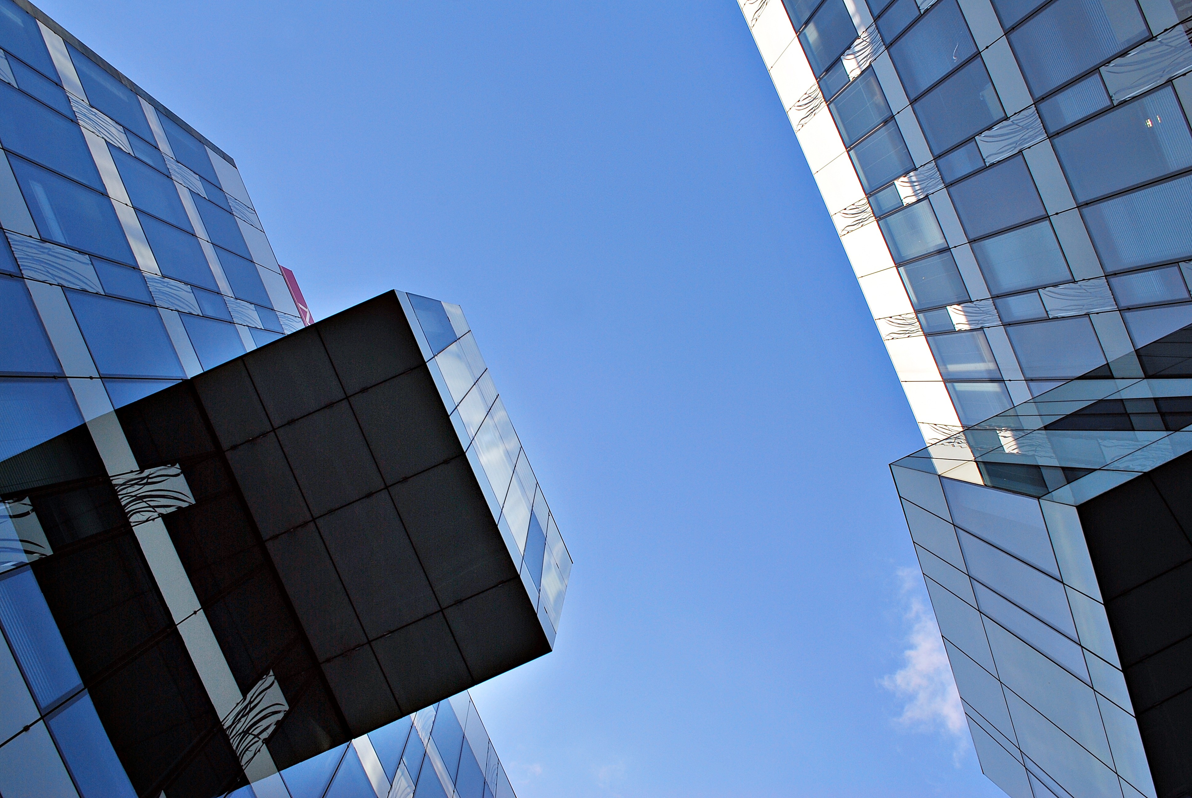 Modern glass skyscrapers viewed from below against a clear blue sky.