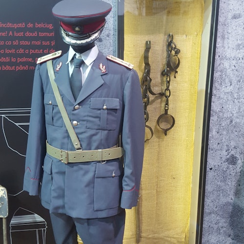 黄色の粗布の背景に、軍服と帽子を着たマネキンと古い手錠の展示が並んでいます。