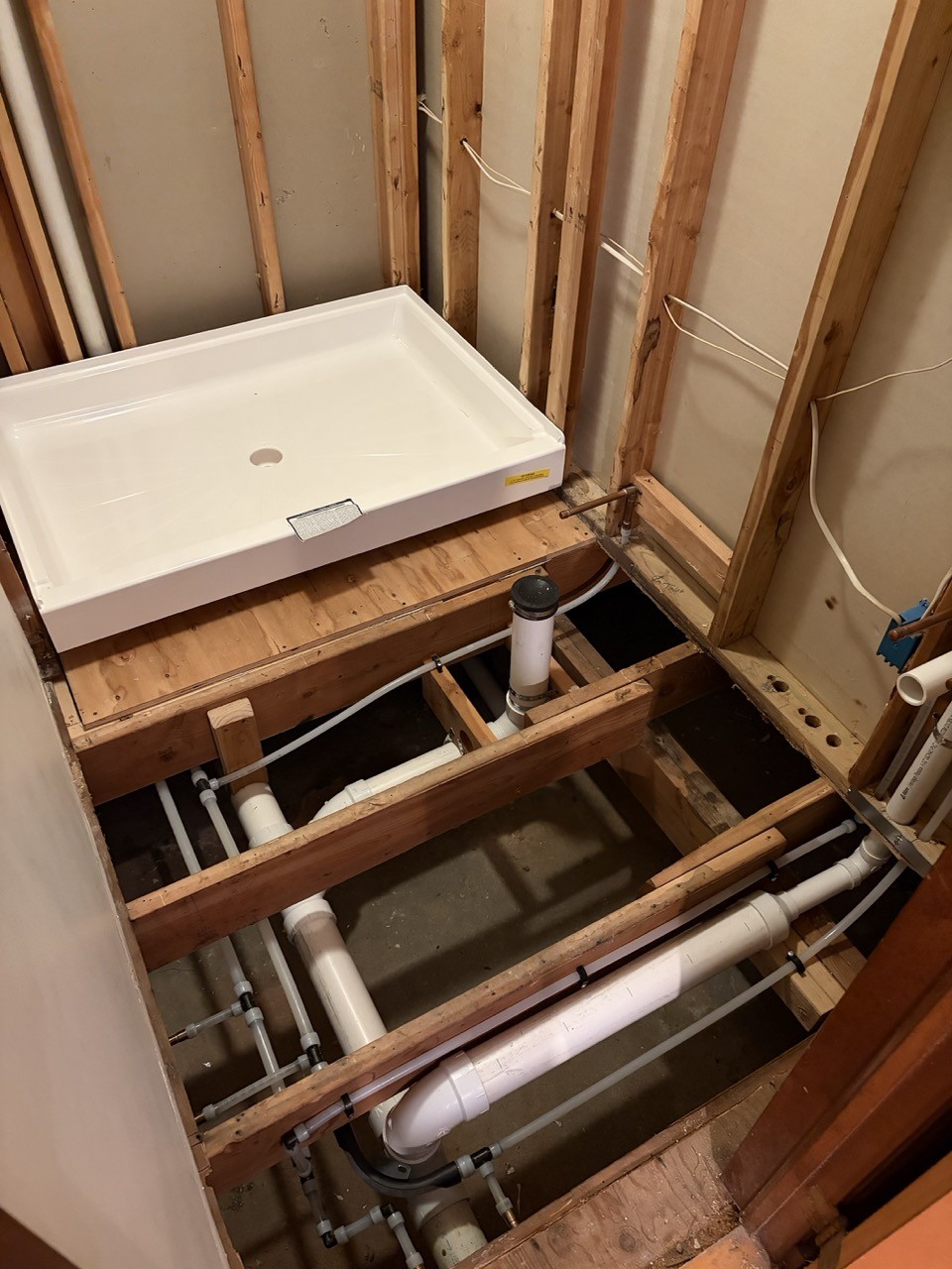 New shower pan set on rebuilt floor framing with new drain and supply lines