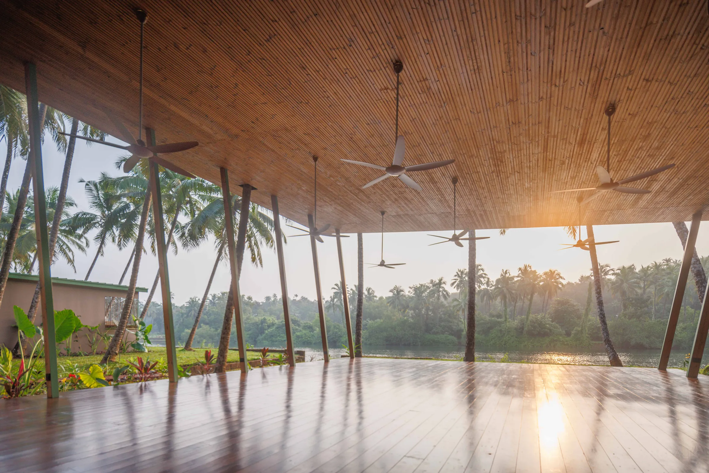 Empty yoga pavilion at sunrise, ceiling fans above and the Talpona River beyond