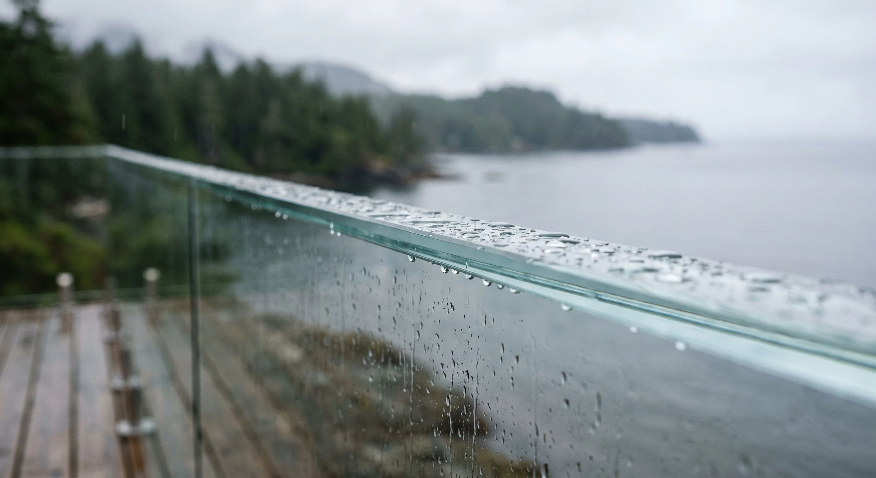 Close view of the exposed top edge of a frameless glass railing panel on a coastal BC deck