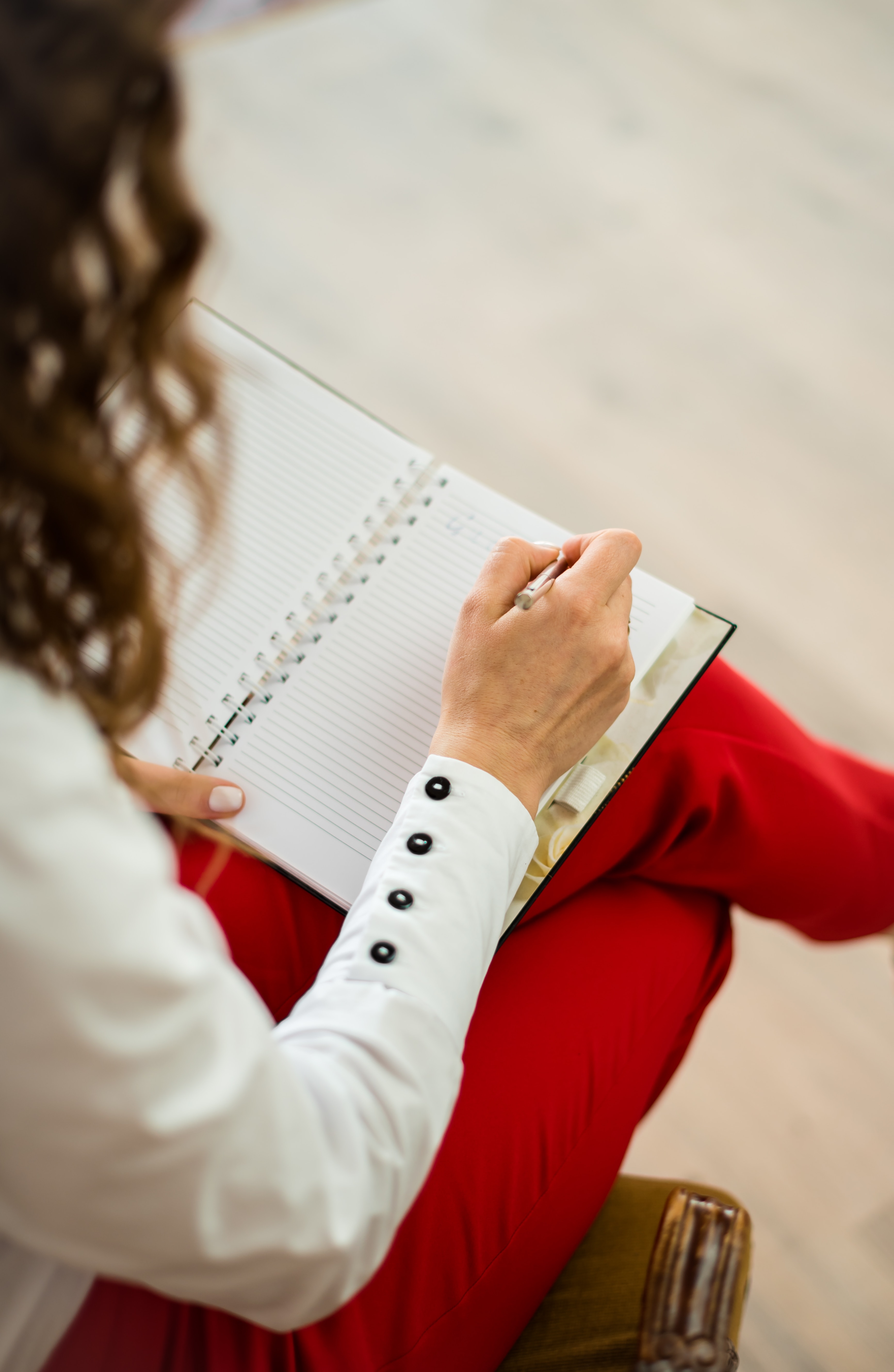 A picture over a woman's shoulder as she writes in a notepad 