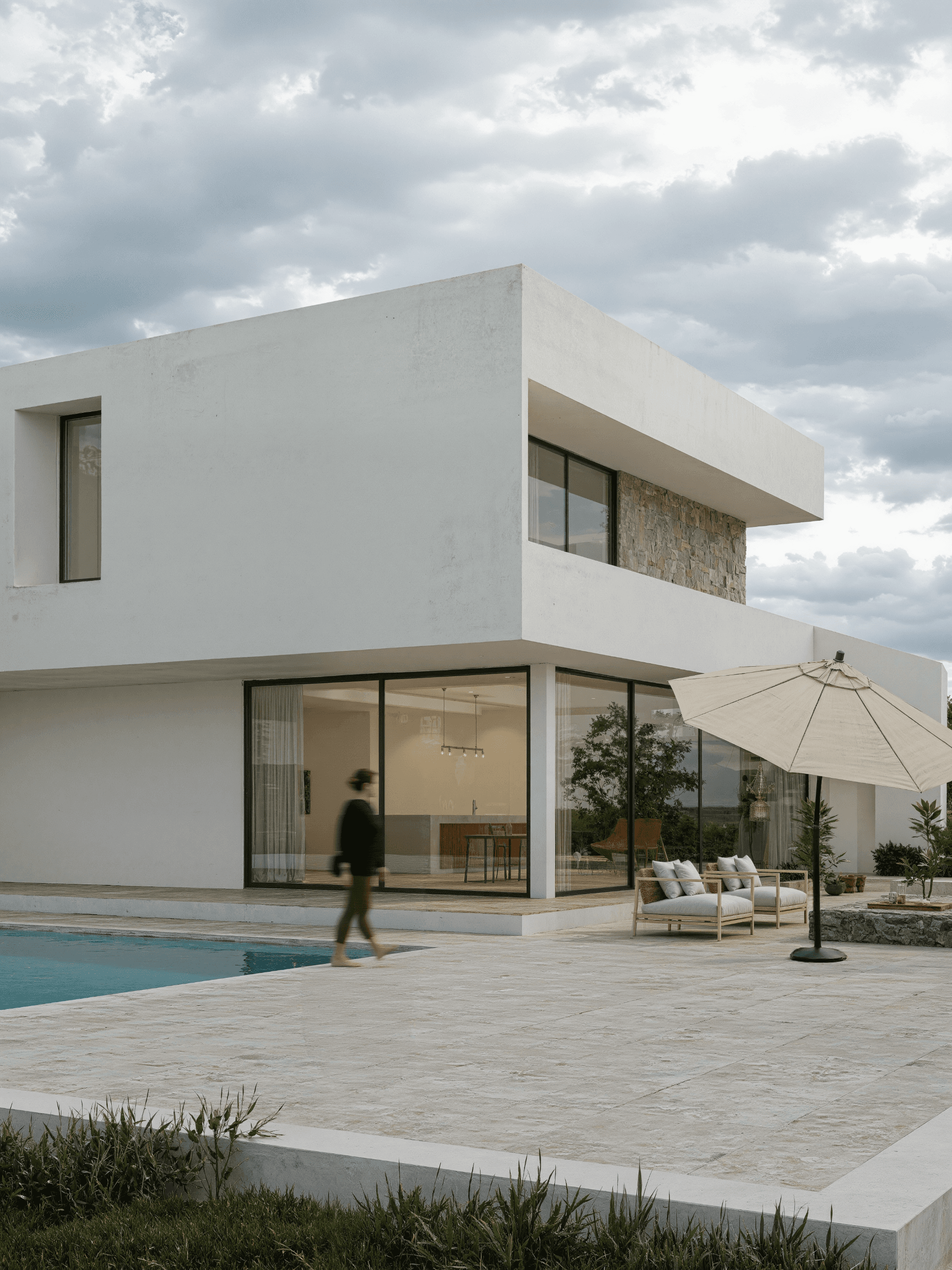 A smiling woman with her arms crossed, standing against a dark green background. She has long, dark hair.