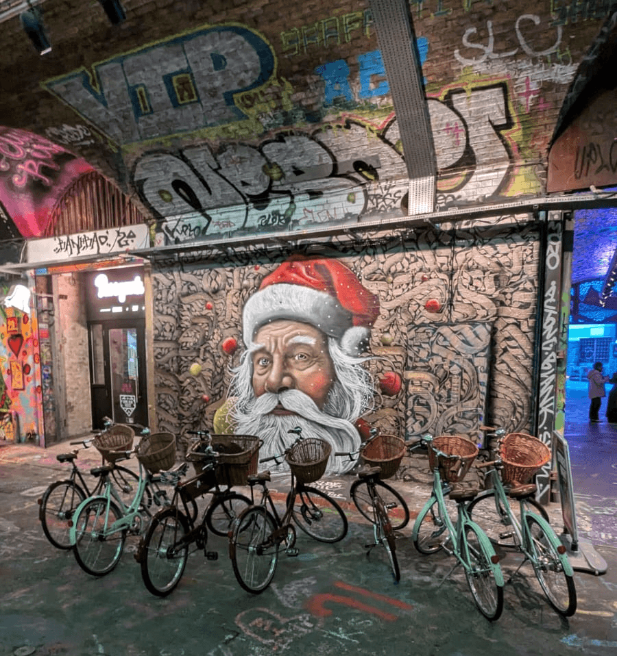 Tally Ho bicycles stopped in front of a mural of Santa in a street art zone, London