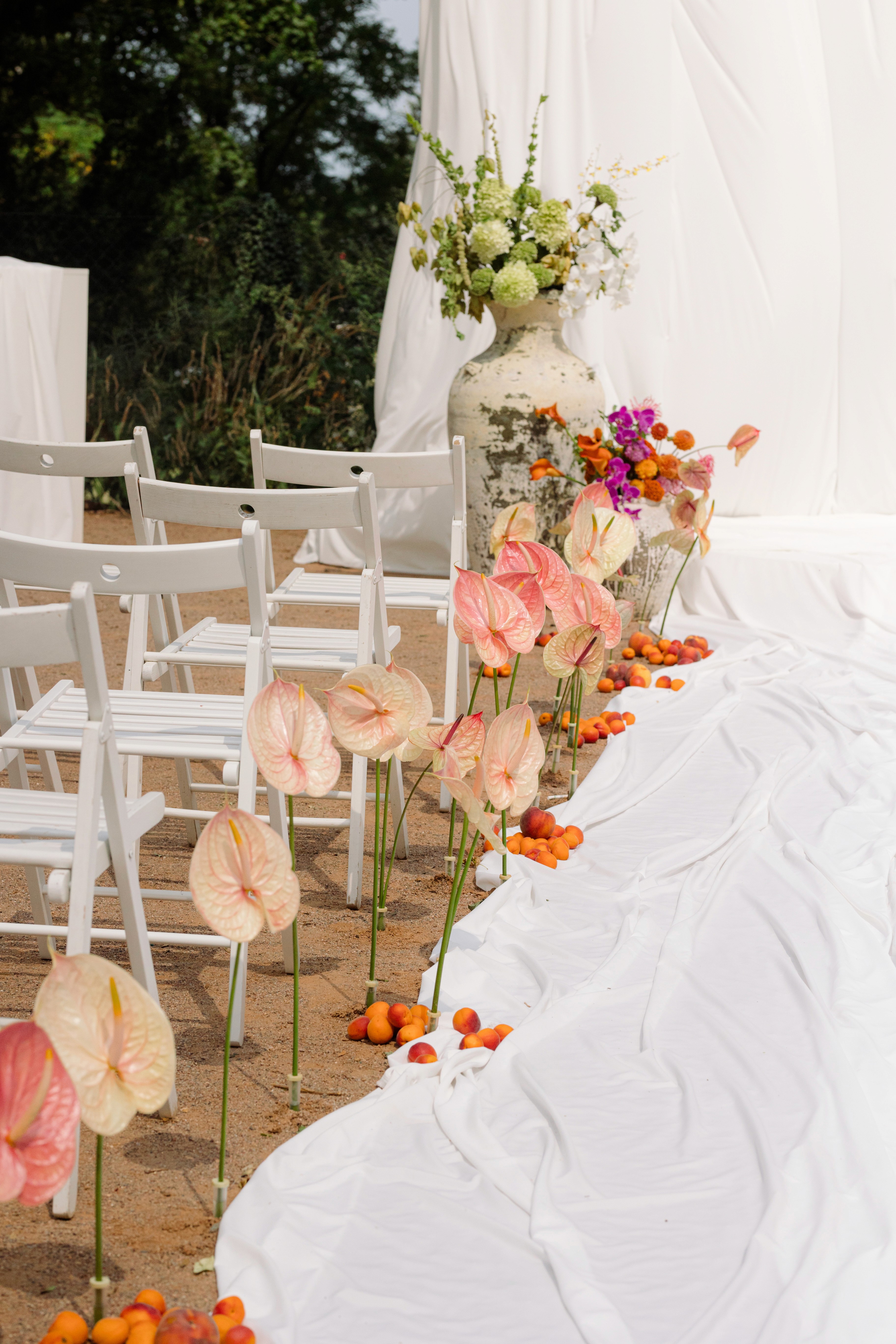 Pastel-toned wedding aisle with tropical flowers and white seating — light, warm, inviting.
