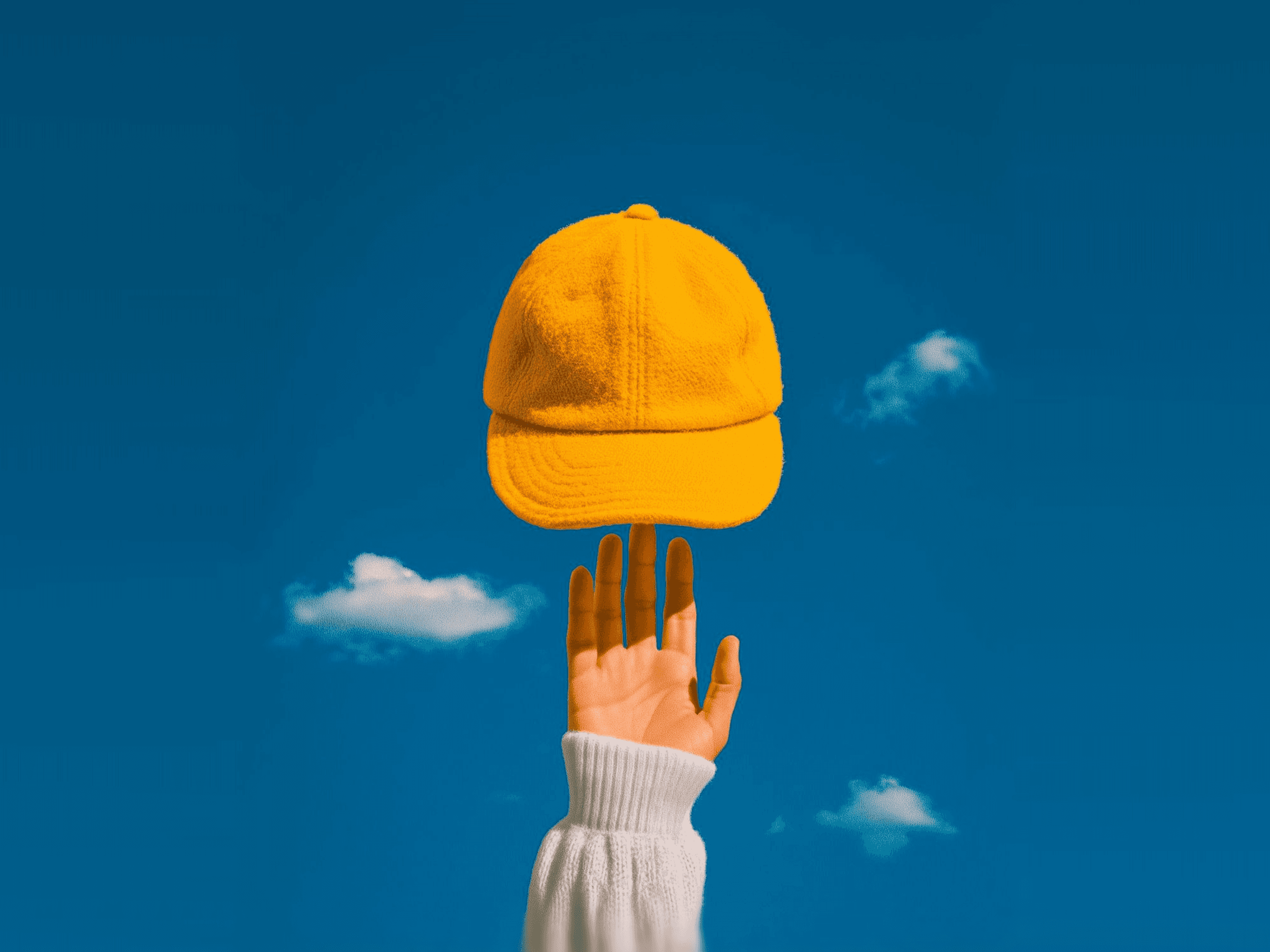 Yellow cap balanced on a finger against blue sky.