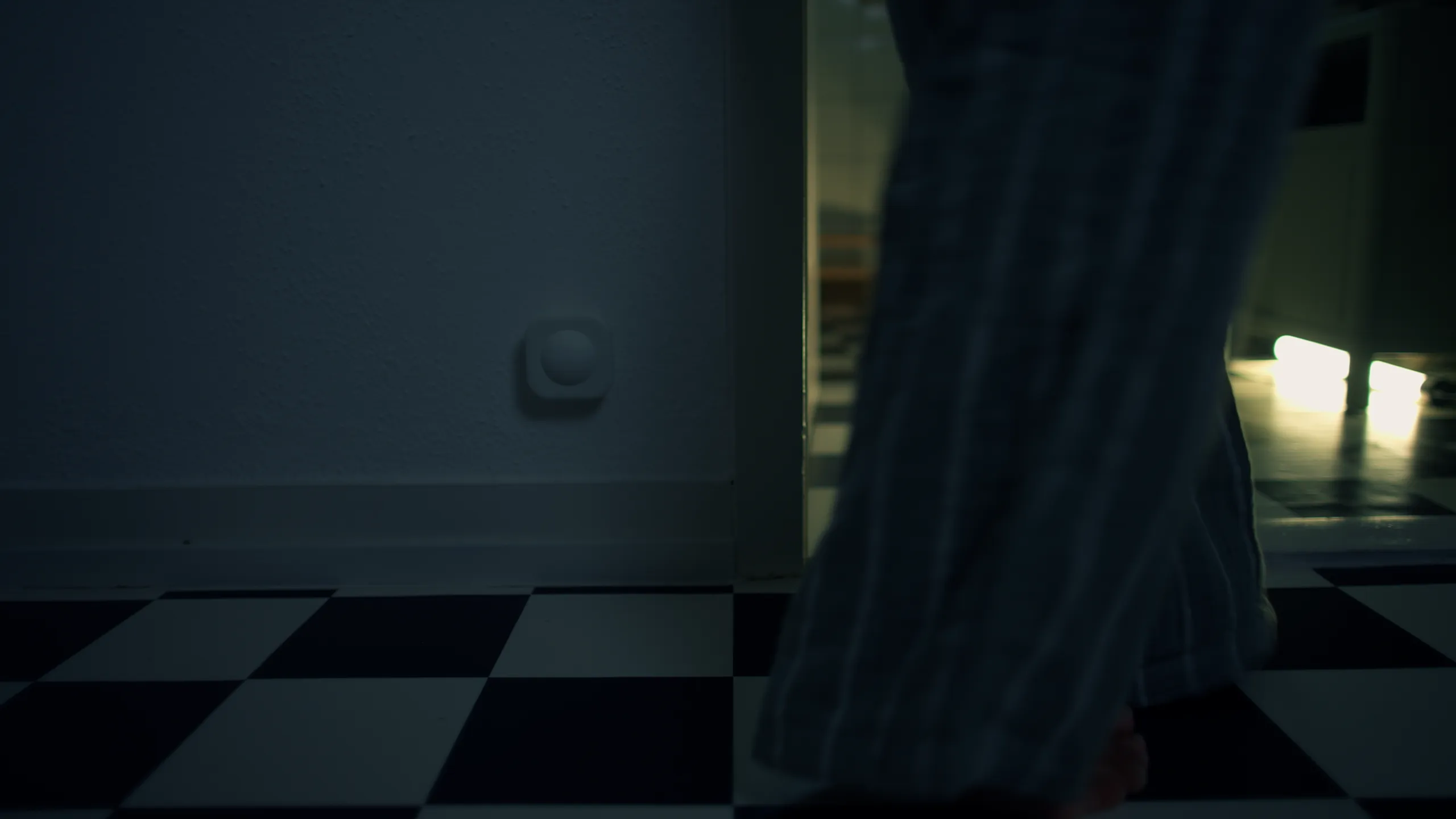 Low angle cinematic shot of striped pajama legs walking across a checkered floor in a dark hallway.