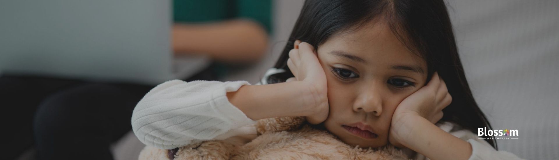 A young girl rests her head on her teddy bear, looking thoughtful and sad.