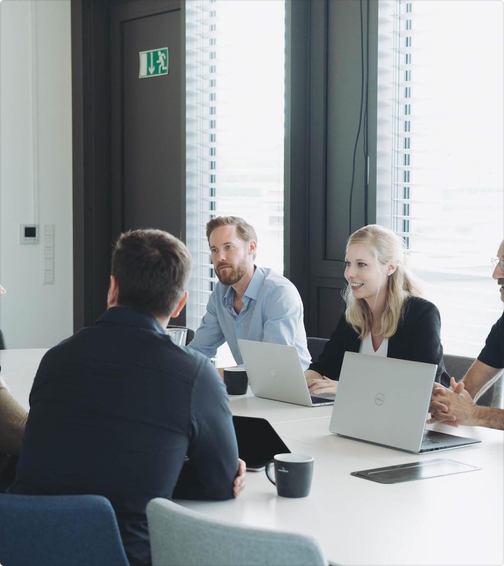 Team diskutiert an einem Tisch mit Laptops.