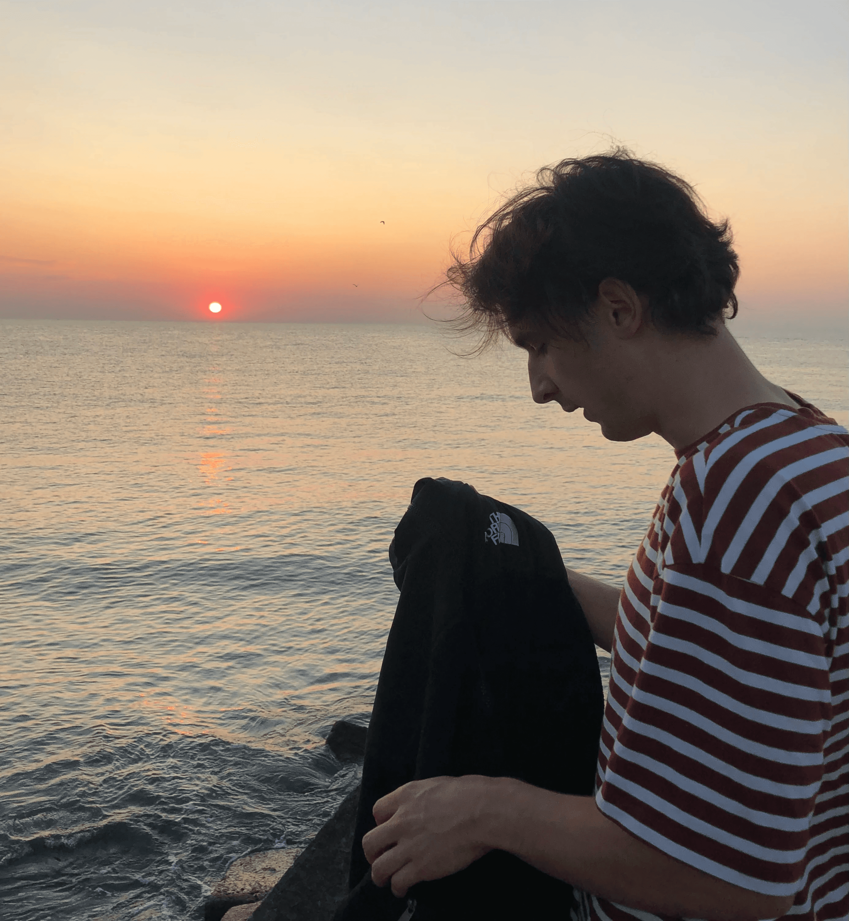 Person wearing a blue puffer jacket and red backpack standing in front of a light blue building on a city street.