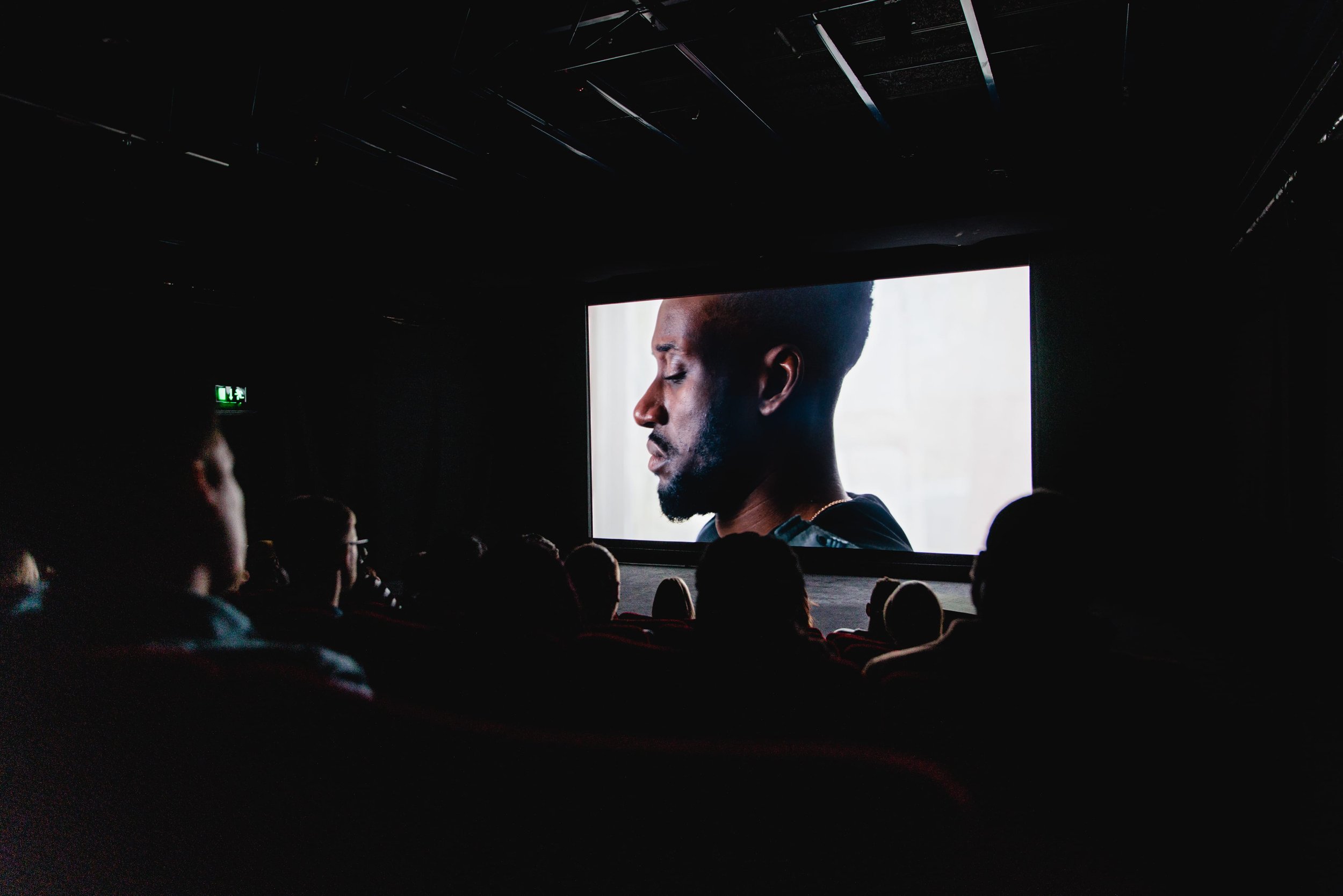 A photograph of the BFI cinema screening of the film "Where I Can See Them," featuring a man on screen on a white background.