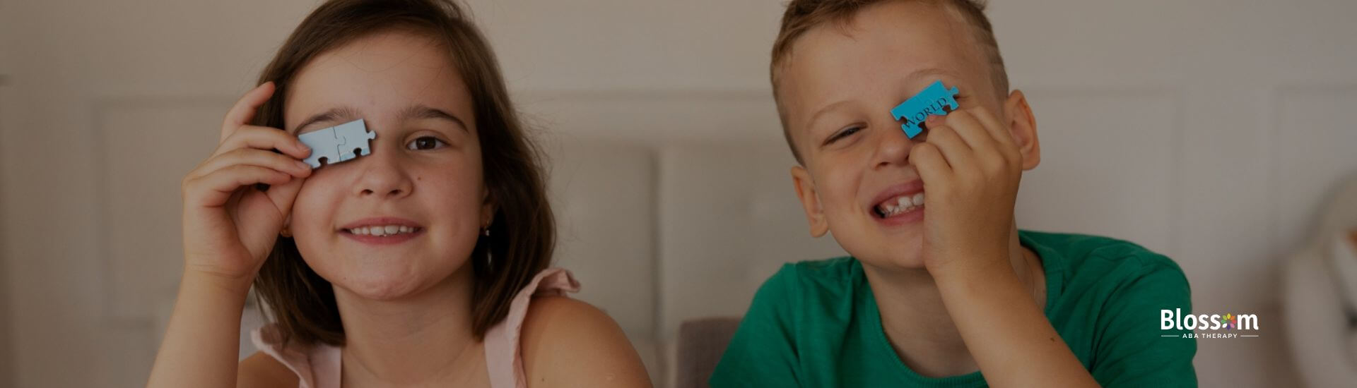 Two children with autism play with puzzle pieces, smiling and holding puzzle pieces up to their eyes.