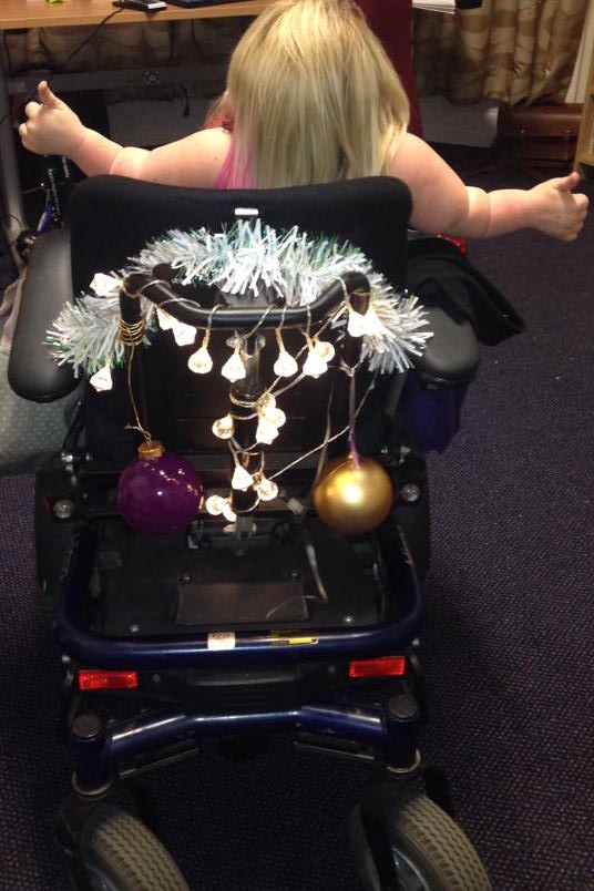 behind shot of Gem's wheelchair dressed festive with Gem's arms and thumbs up