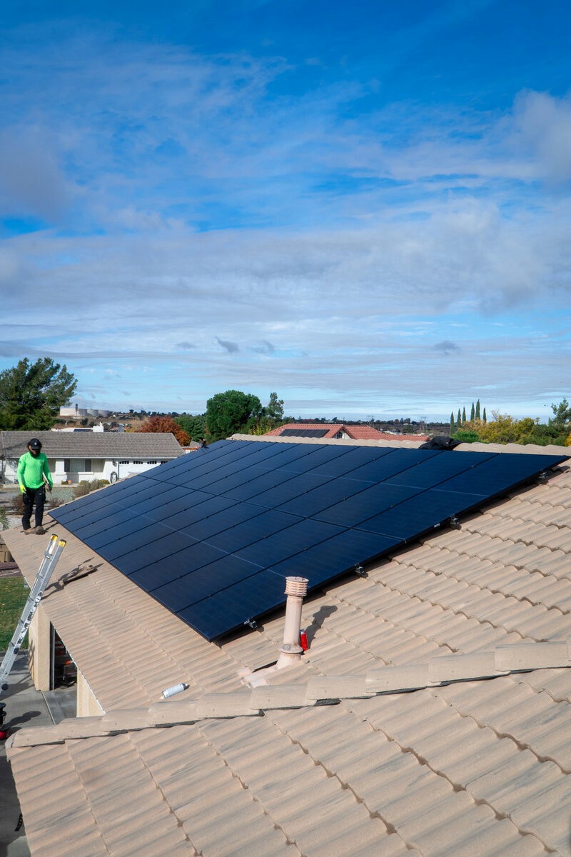 Black solar panels on the gray tile roof of a Southern California home, with an Option One installer at the roof edge