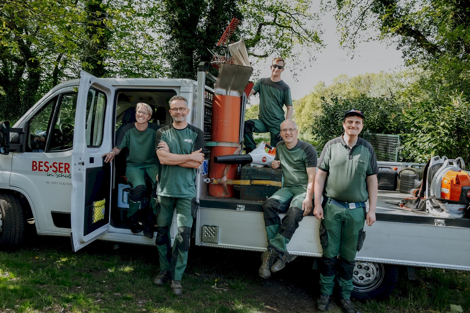 Ein Team von Gärtnern posiert vor einem weißen Transporter. Sie tragen grüne Arbeitskleidung. 