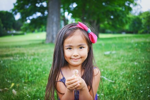 A young Vietnamese girl sitting in grass with a flower in her hand