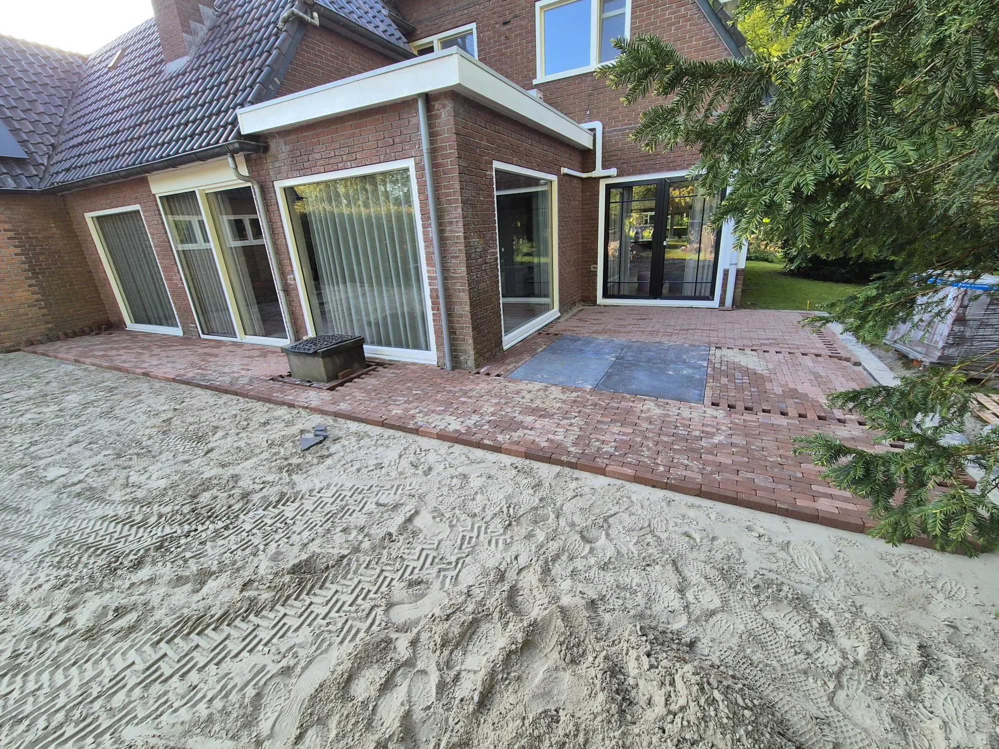 Rustiek terras in aanbouw met oud Hollandse tegels en gebakken klinkers, trap naar lagere tuin bij woning in Oldeberkoop.