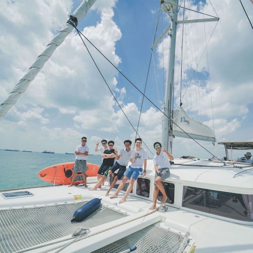 五个人在多云的天空下乘坐帆船。他们坐着或站在船上的缆绳附近，可以看到一艘救生艇。