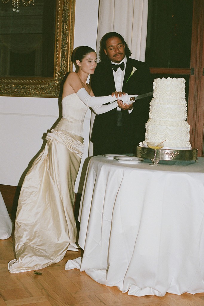 Bride and groom cutting a tiered vintage wedding cake during an indoor wedding reception