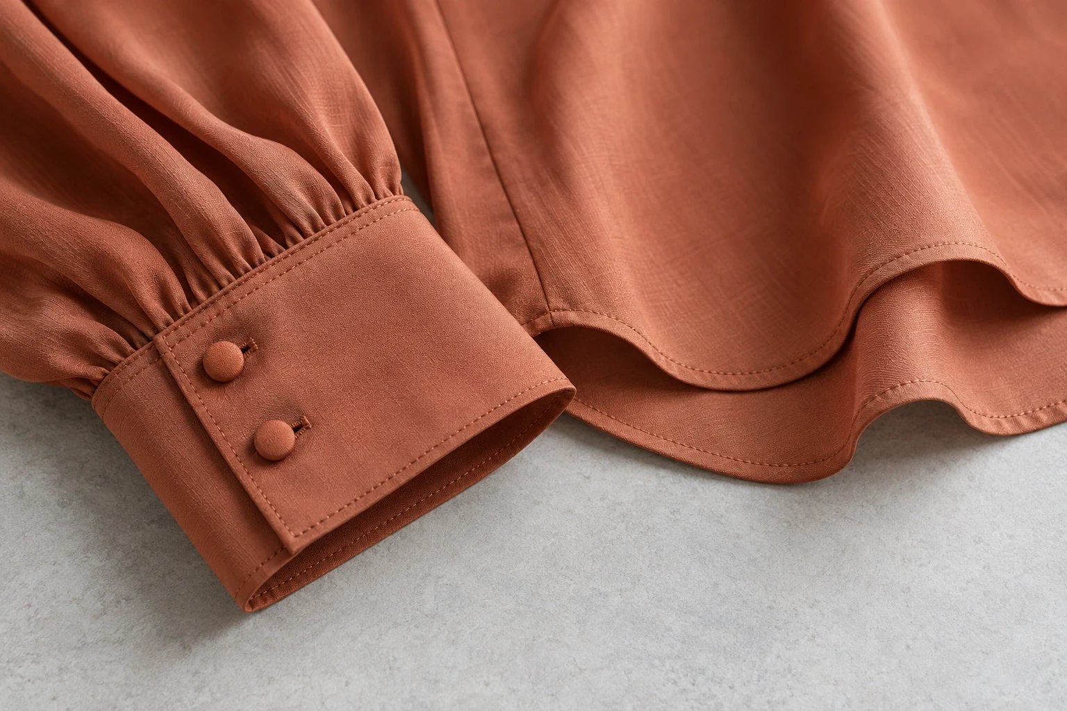 Close view of a terracotta blouse cuff, matching buttons and a folded hem