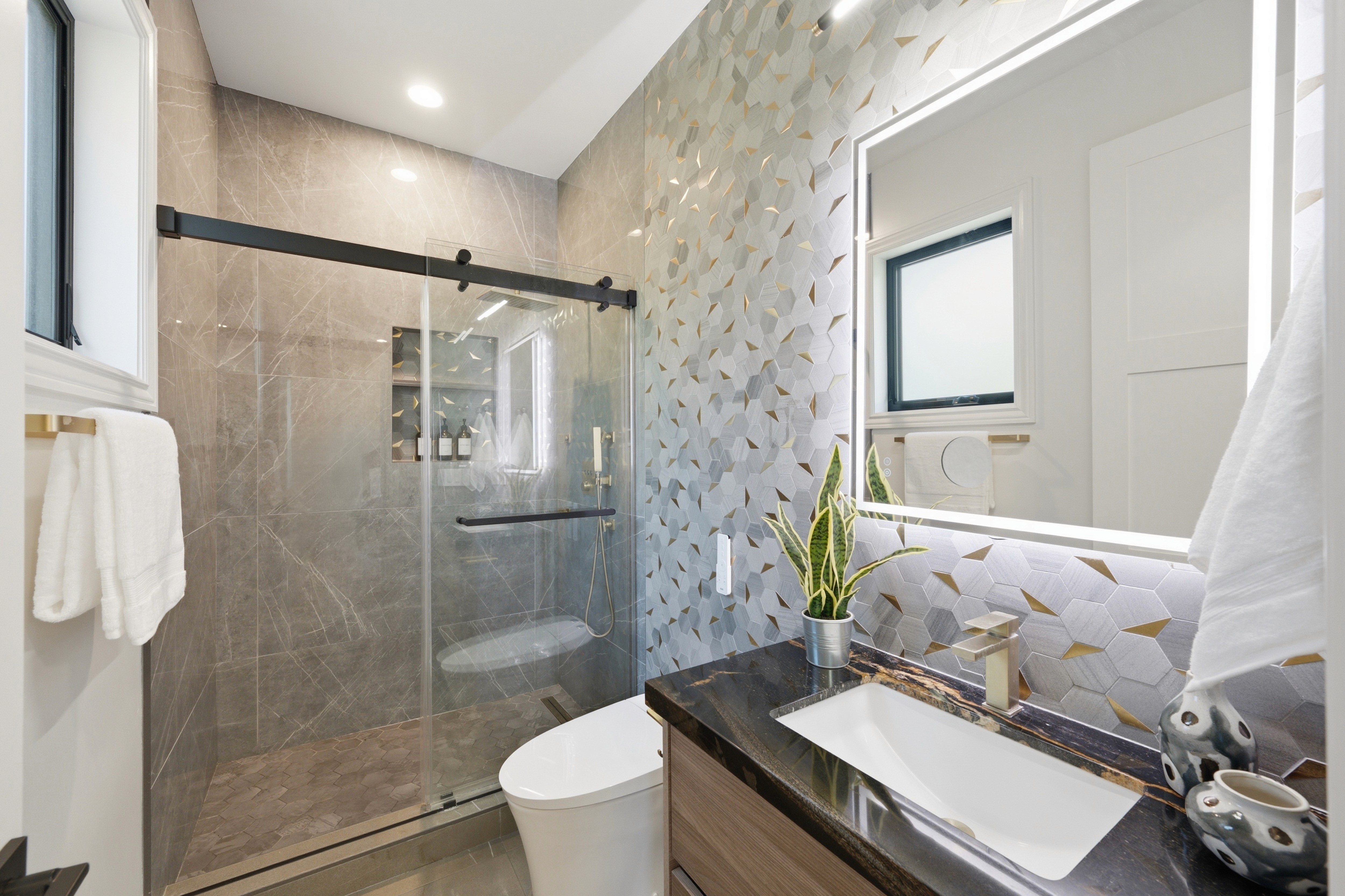 Bathroom with a sliding glass shower door, dark stone vanity, and backlit mirror.