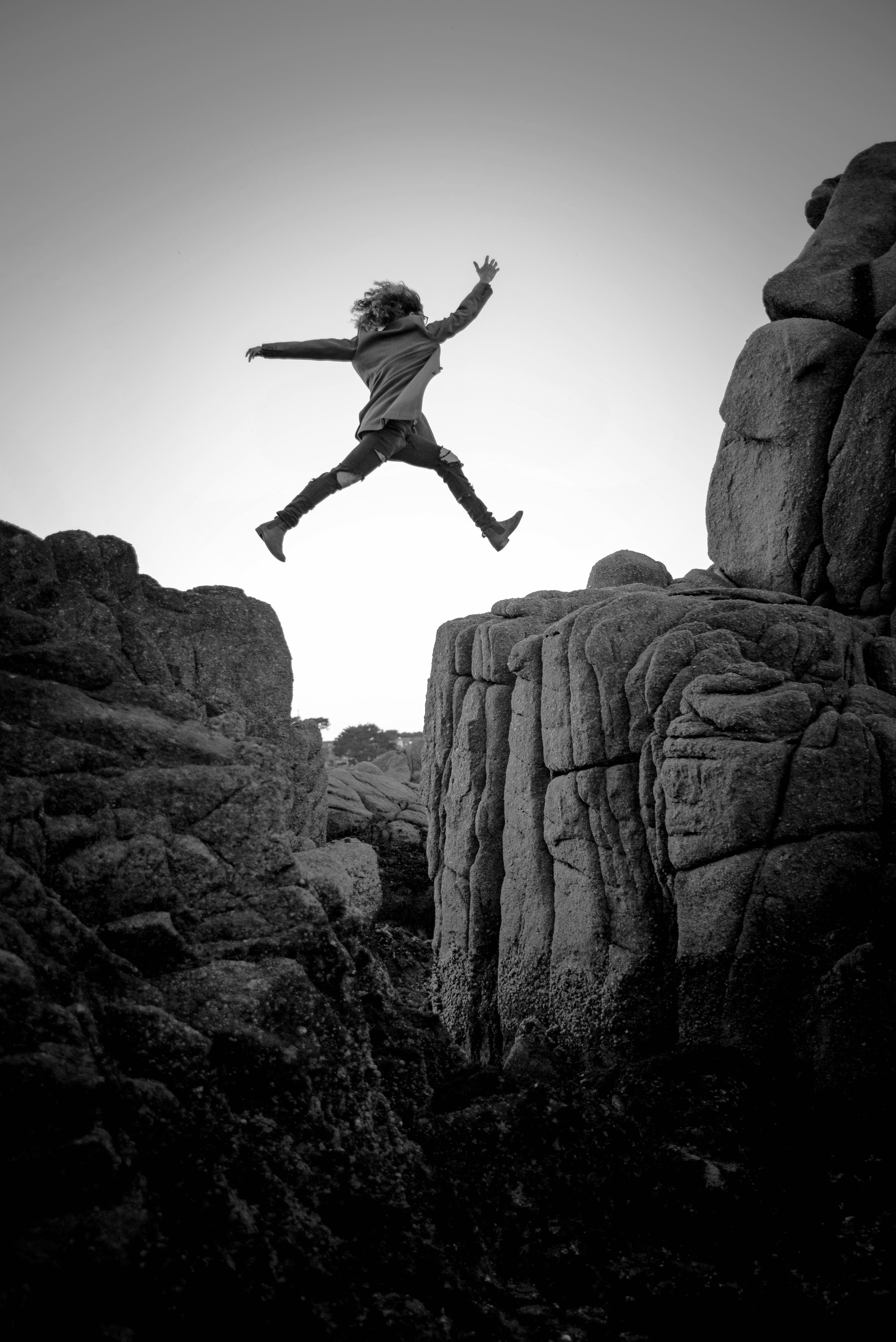 person jumping on big rock under gray and white sky during daytime