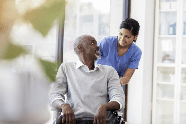 A care worker assisting an elderly man in an indoor care setting, providing personal support