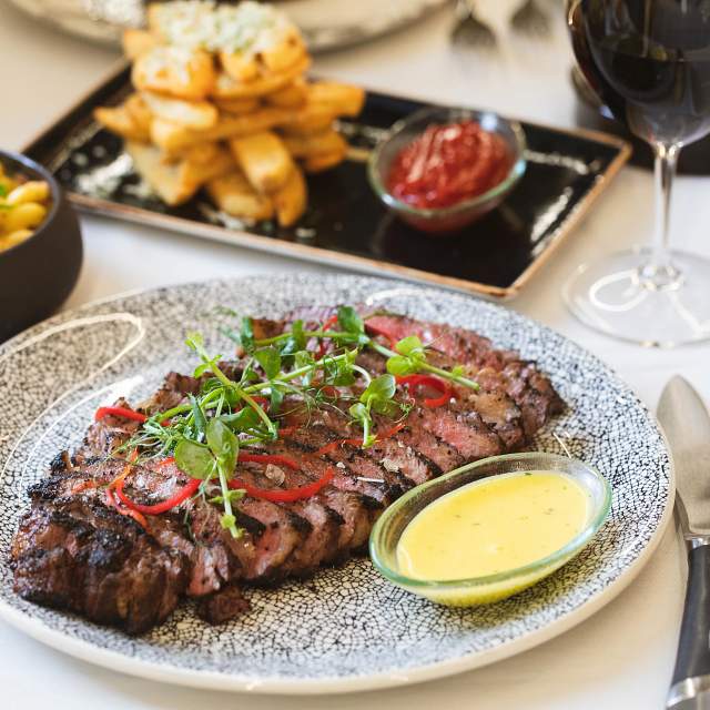 Sliced grilled steak on a speckled plate with bearnaise sauce, potatoes, and ketchup in the background.