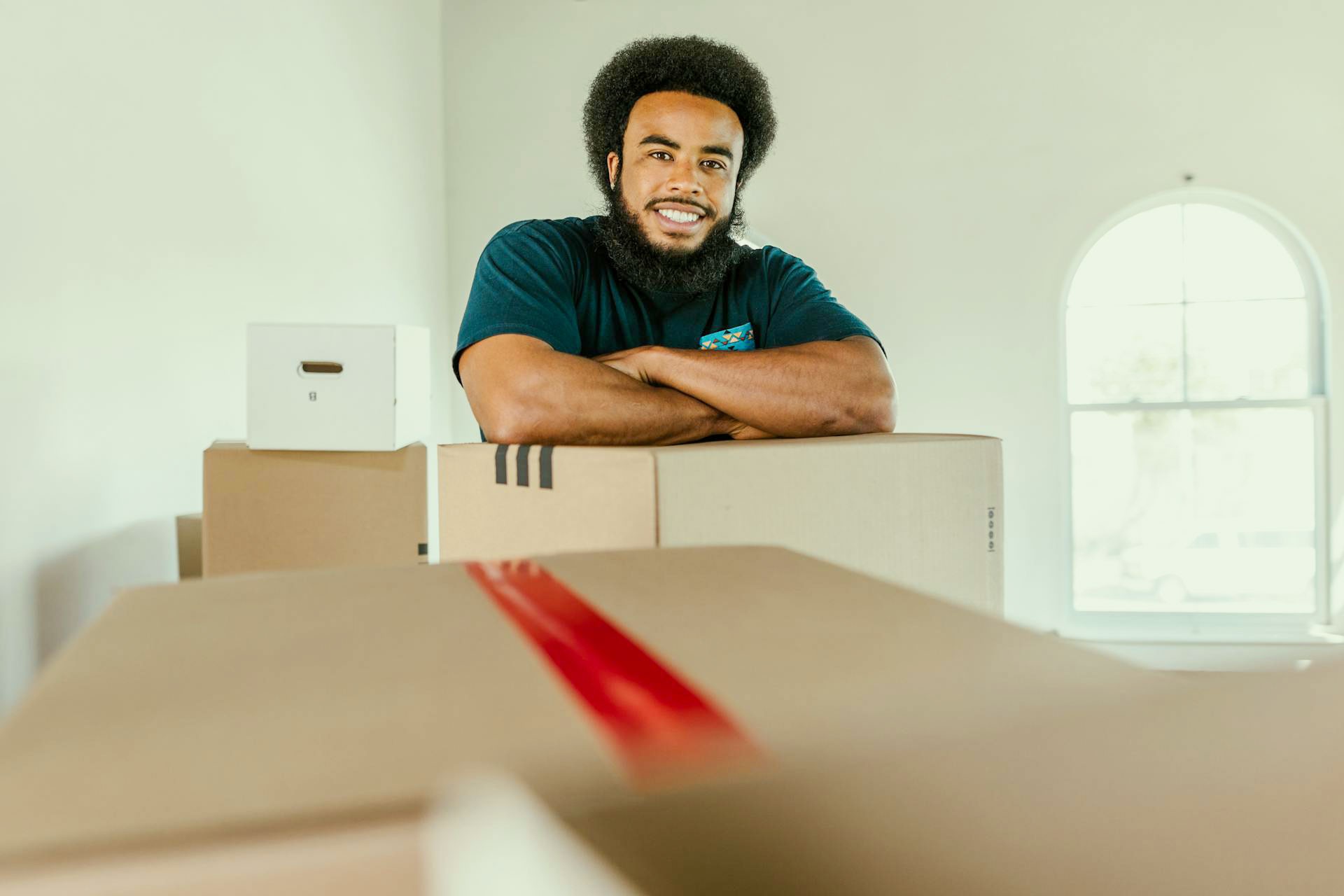 A Male moving company worker surrounded by boxes, smilling to the camera.