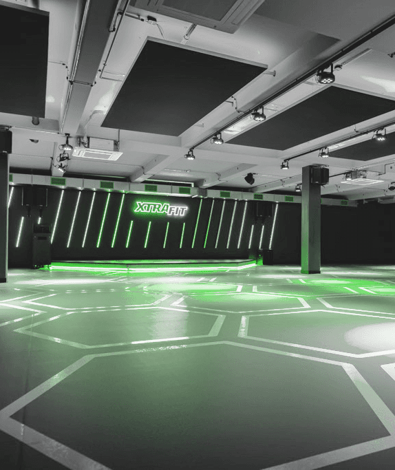 Neonbeleuchteter Kursraum im XTRAFIT Fitnessstudio mit hexagonalen Mustern und moderner Bühne.